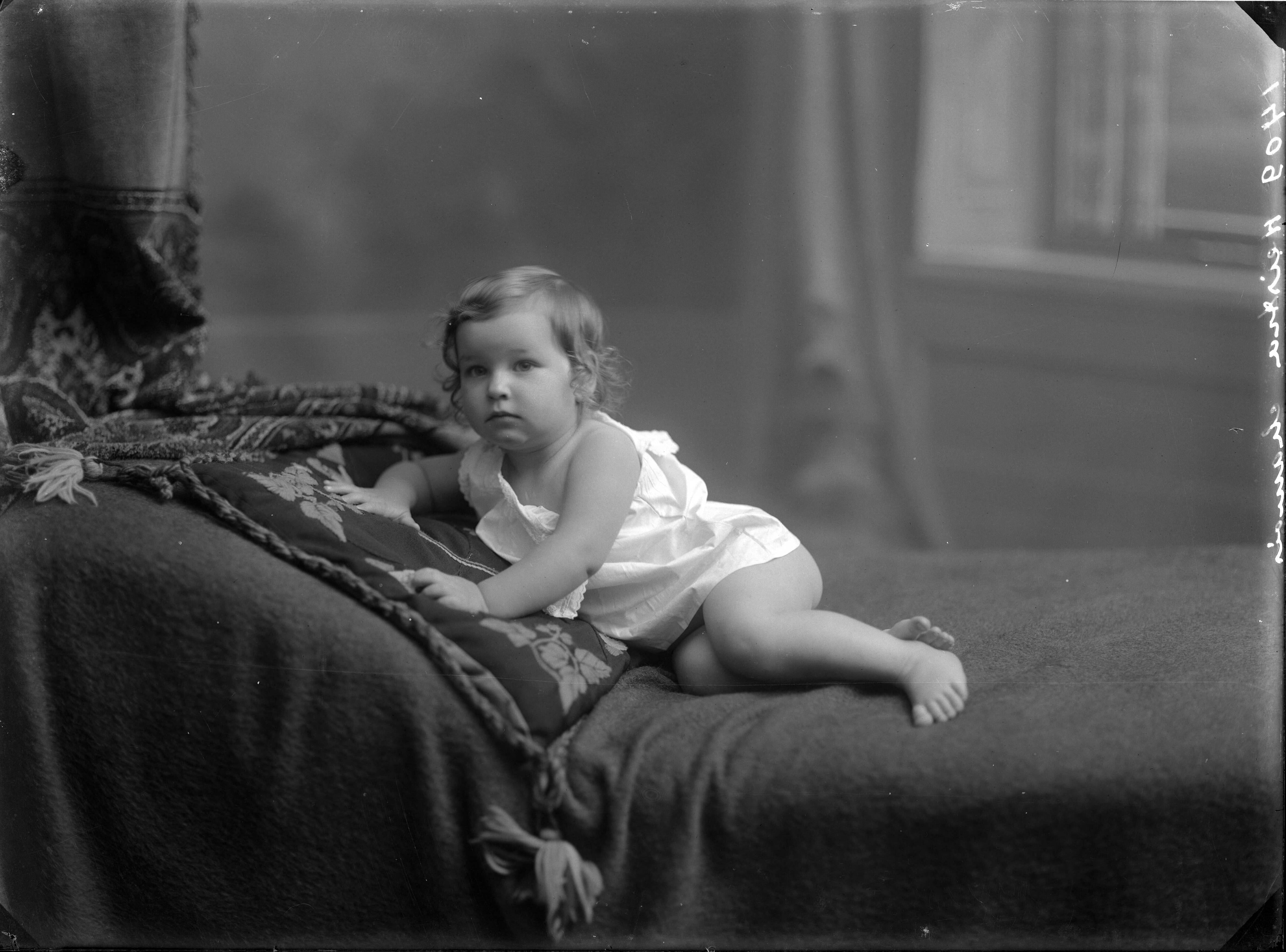 Berg, van den (BERG 050) — Studio-opnames. Babymeisje in wit hemdjurkje op smyrna-kussen met een ontblote schouder tegen leuning van een bank. Haarlem, Nederland. 1918-1930. 1409 Heistra chamois — Foto: Berg, Th.C.J. van den / Spaarnestad Photo (05887). Licentie: Set B: Rechtenvrij / Publiek Domein. Bron: Nationaal Archief. http://hdl.handle.net/10648/35429da7-c774-a382-e063-6df0900a6686