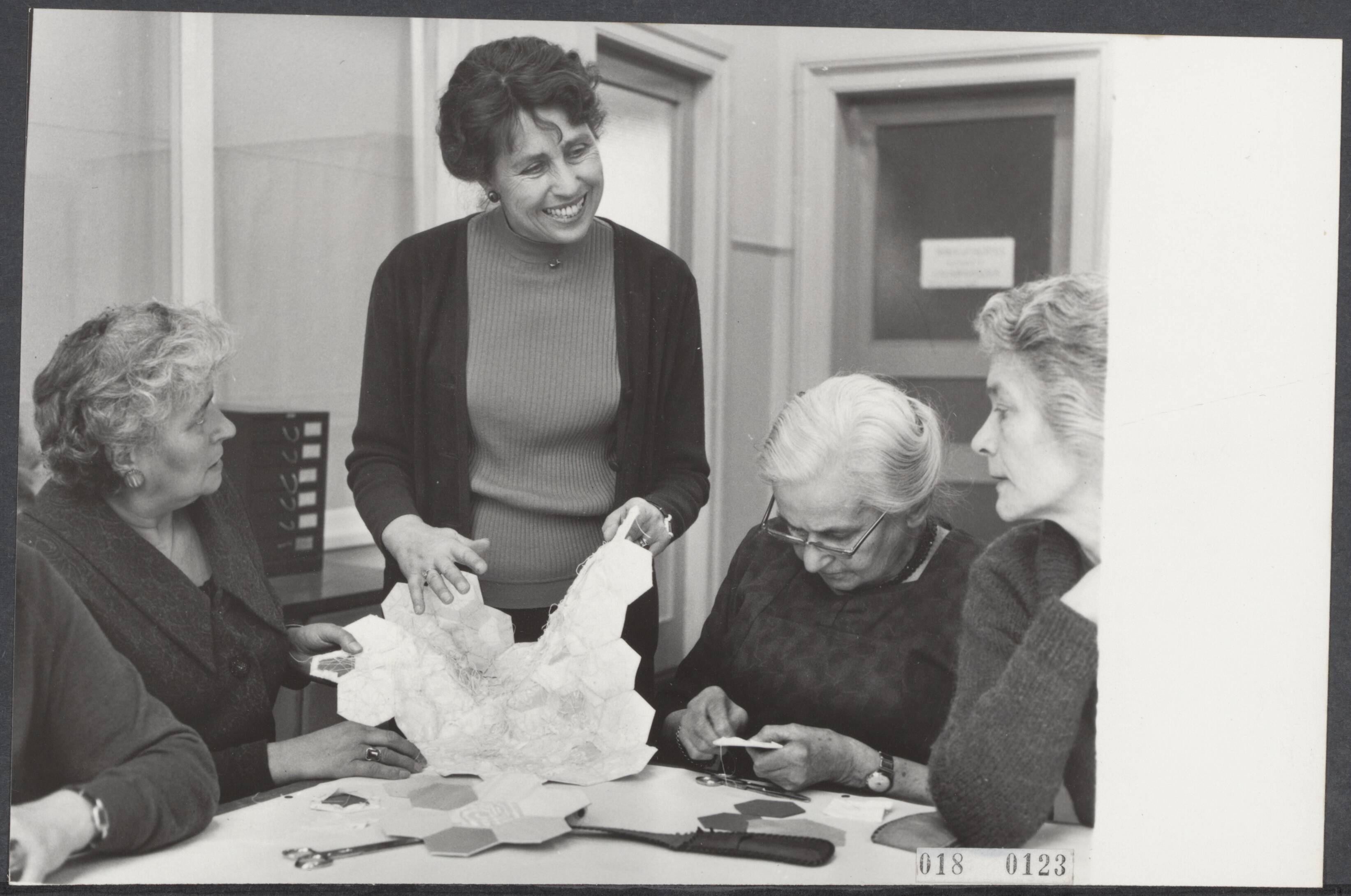 Fotocollectie Elsevier Binnenland — Voorbereidingen huwelijk prinses Beatrix en Claus von Amsberg. In Haarlem zijn vrijwilligers in de werkplaats tot herstel van antiek textiel begonnen aan het vervaardigen van een sprei voor prinses Beatrix. Het idee is van de echtgenote van de burgemeester van Haarlem, mevr. Cremers-De Bruijn. De artistieke leiding berust bij mevr. Verwij. Mevrouw Cremers-de Bruijn toont de vrijwilligers een voorbeeld — Foto: Kroon, Ron / Anefo. Licentie: Set B: Rechtenvrij / Publiek Domein. Bron: Nationaal Archief. http://hdl.handle.net/10648/adc14944-d0b4-102d-bcf8-003048976d84