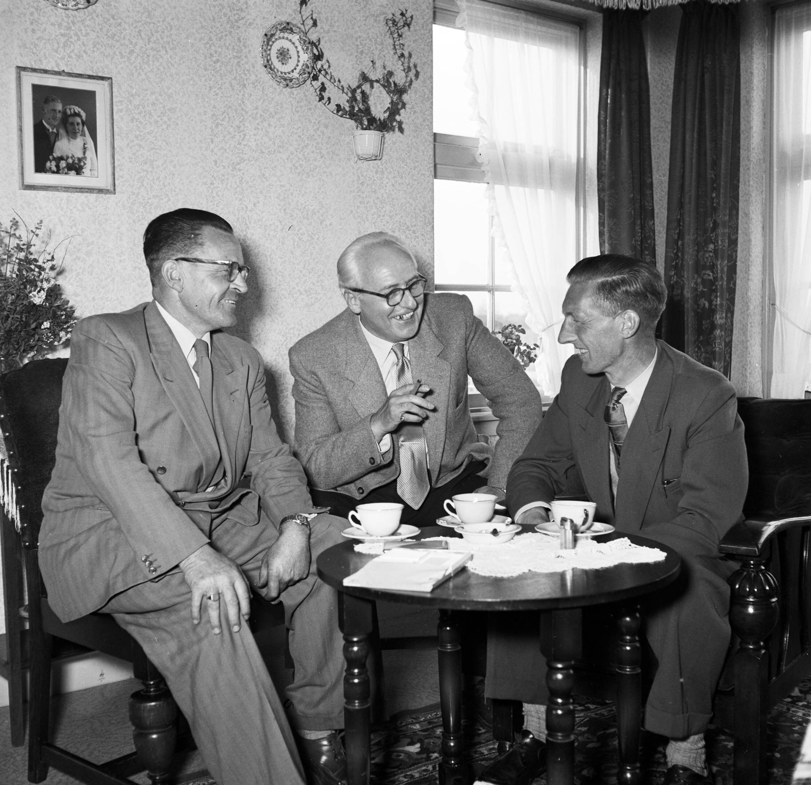 Fotocollectie Van de Poll — Gerard de Jong in gesprek met Ynse Postma en de fotograaf Willem van de Poll. Aan de wand een trouwfoto van het echtpaar De Jong — Foto: Poll, Willem van de. Licentie: Set B: Rechtenvrij / Publiek Domein. Bron: Nationaal Archief. http://hdl.handle.net/10648/aeccea28-d0b4-102d-bcf8-003048976d84