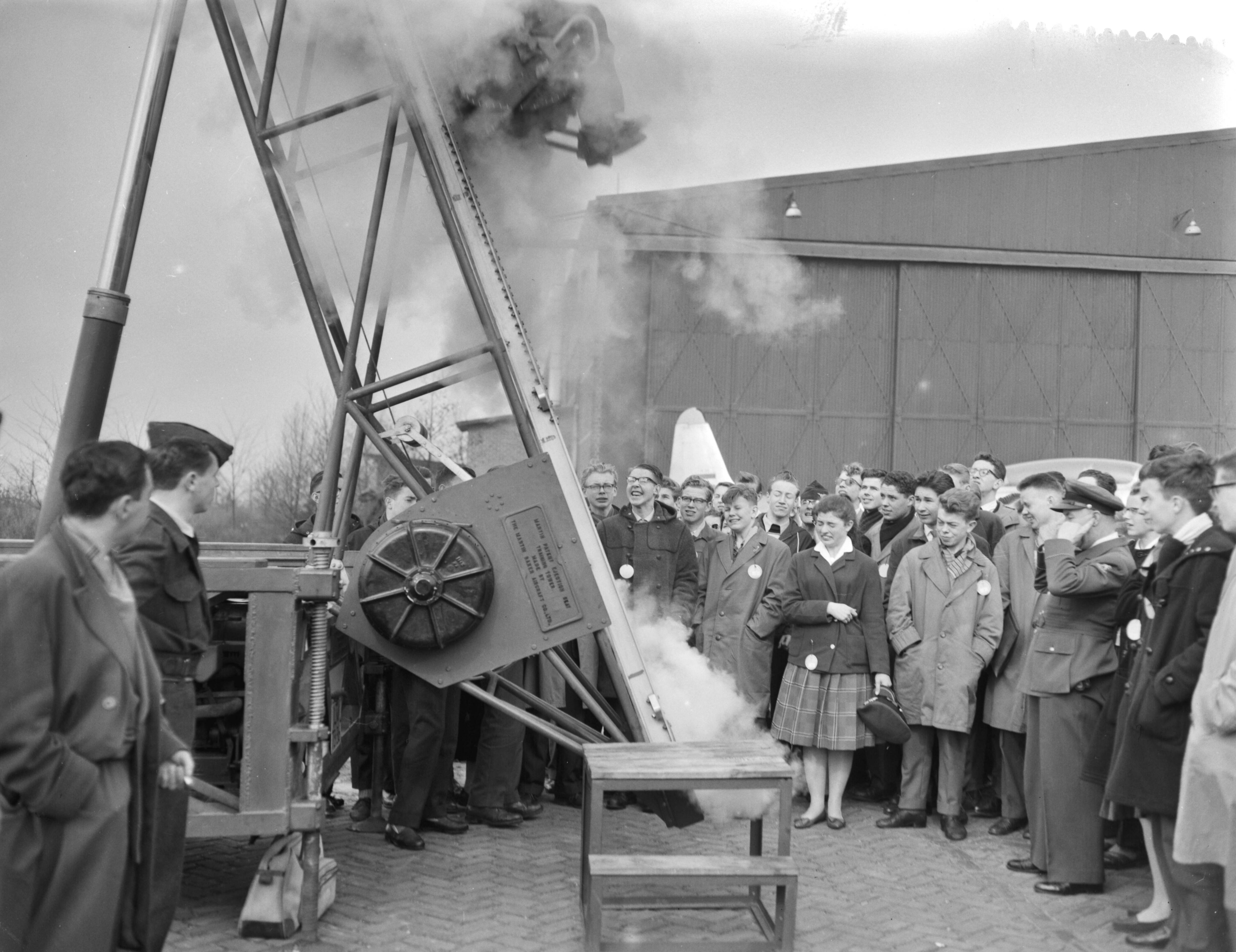 Fotocollectie Anefo — Nationale Luchtvaartdag op Soesterberg. Majoor M. E. J. A. Smitshuysen , hoofd LVD, demonstreert schietstoel — Foto: Rossem, Wim van / Anefo. Licentie: Set B: Rechtenvrij / Publiek Domein. Bron: Nationaal Archief. http://hdl.handle.net/10648/a990b558-d0b4-102d-bcf8-003048976d84