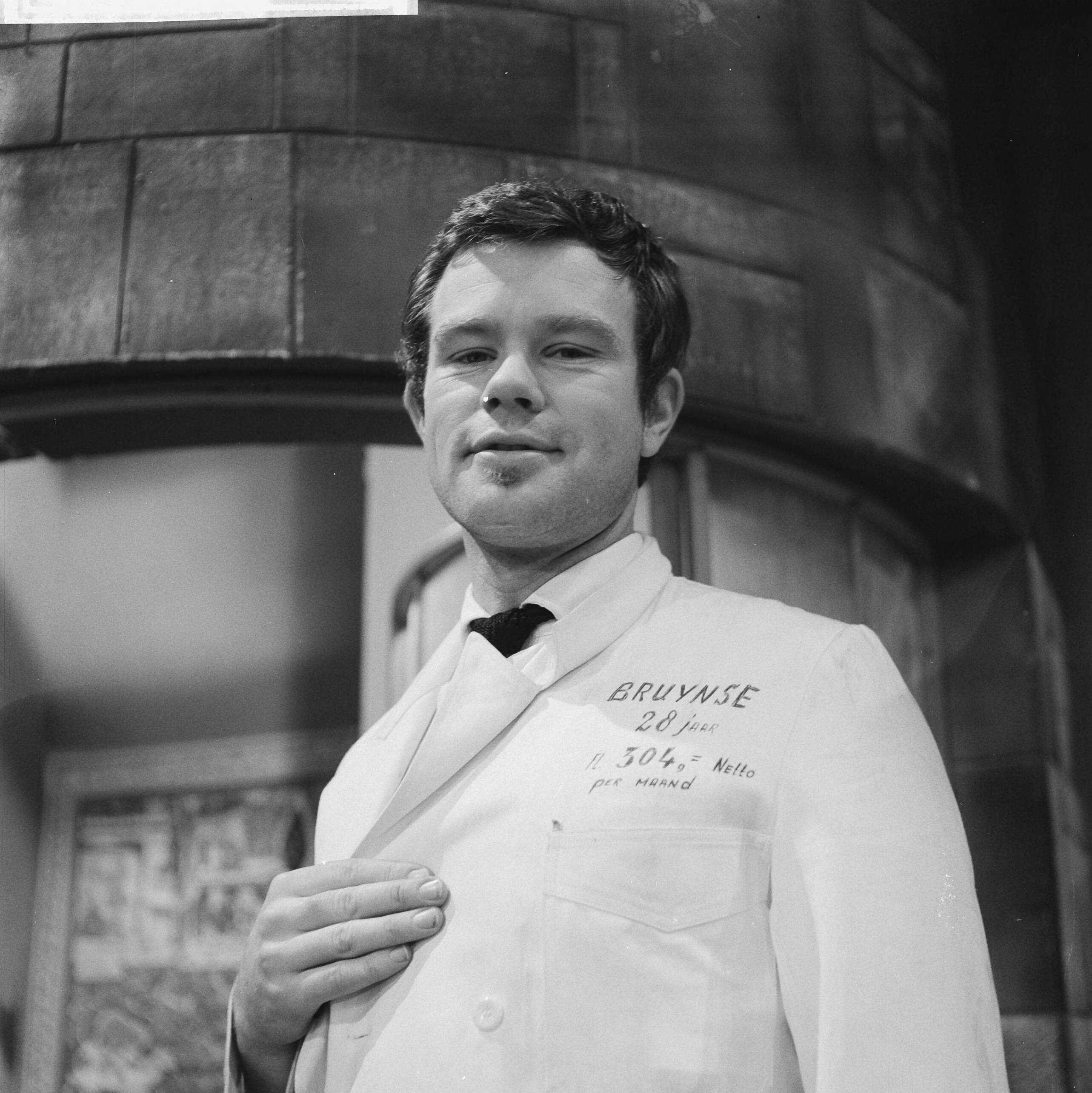 Fotocollectie Anefo — Ontevreden toneelmeesters bij NTS. Toneelmeester met grieven geschreven op stofjas — Foto: Lindeboom, Henk / Anefo. Licentie: Set B: Rechtenvrij / Publiek Domein. Bron: Nationaal Archief. http://hdl.handle.net/10648/a9ed9ed0-d0b4-102d-bcf8-003048976d84