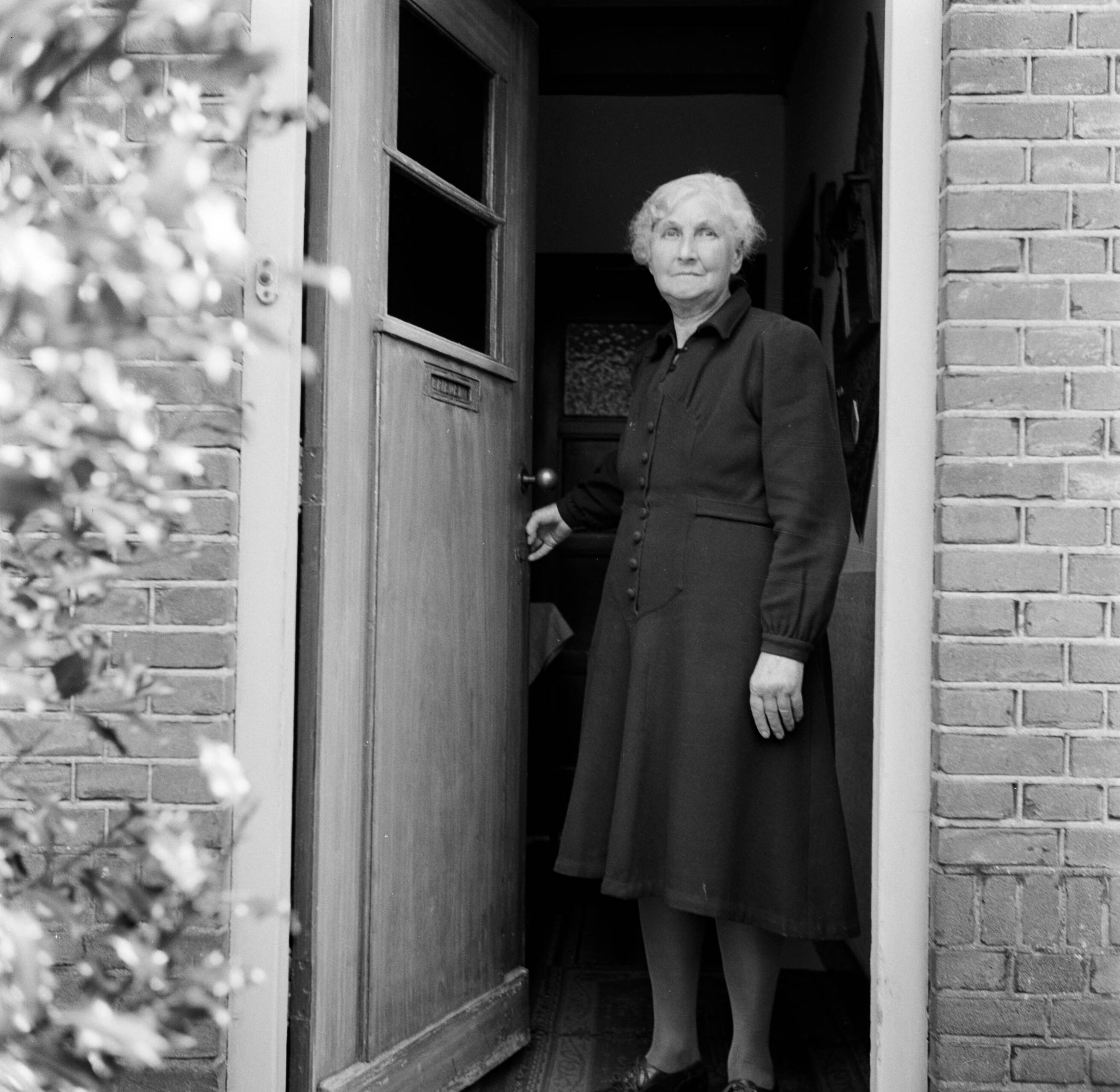 Fotocollectie Van de Poll — Moeder De Jong in de deuropening van hun woning in Huizum (nu deel van Leeuwarden) — Foto: Poll, Willem van de. Licentie: Set B: Rechtenvrij / Publiek Domein. Bron: Nationaal Archief. http://hdl.handle.net/10648/aeccc962-d0b4-102d-bcf8-003048976d84