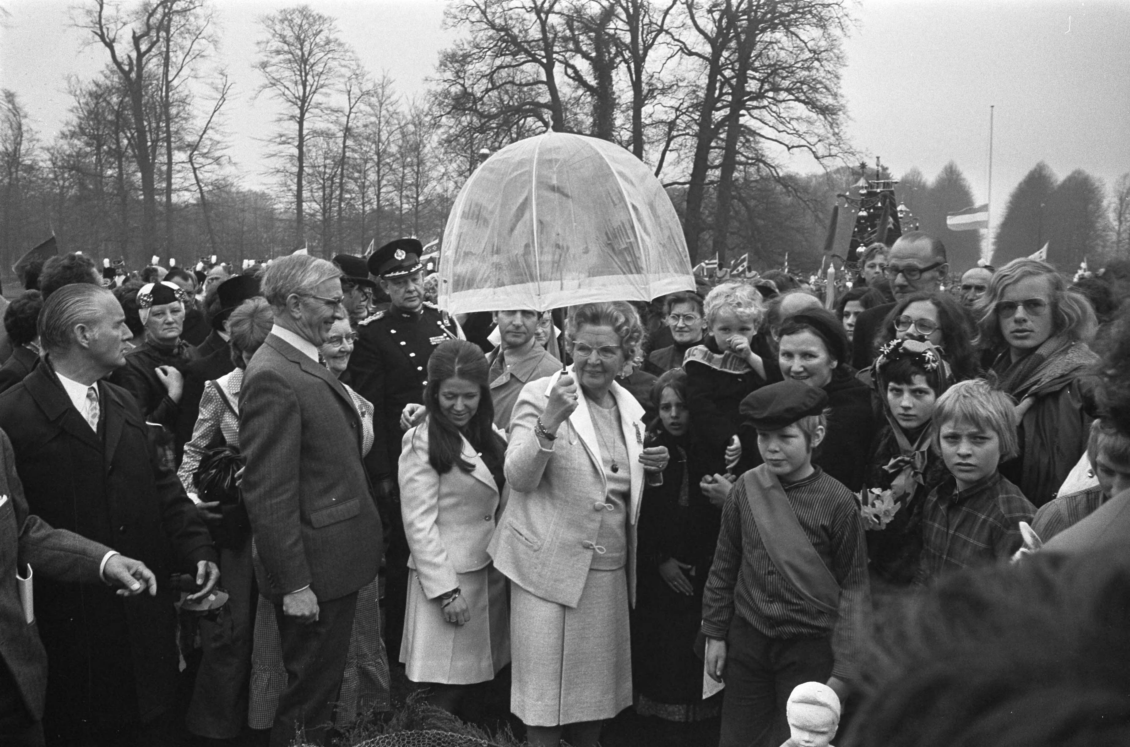 Koninginnedag 1973 — Koningin Juliana en prinses Christina onder de paraplu in de tuin. Naast de koningin staat de jonge acteur die het personage Bartje speelt in de gelijknamige tv-serie, met diens moeder — Foto: Fotograaf Onbekend / Anefo. Licentie: Set B: Rechtenvrij / Publiek Domein. Bron: Nationaal Archief. http://hdl.handle.net/10648/ac2afa12-d0b4-102d-bcf8-003048976d84