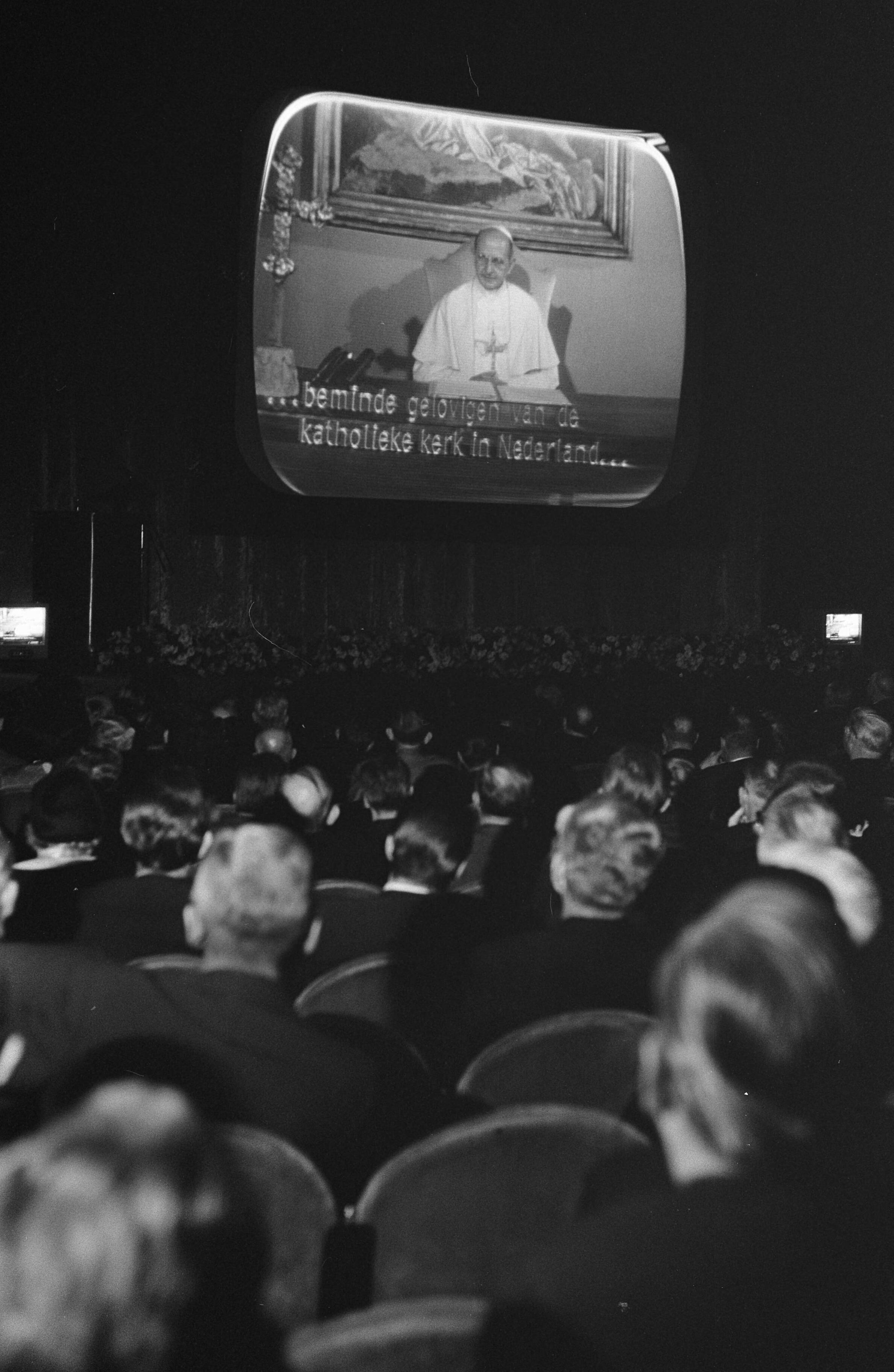 Viering van het veertigjarig bestaan van de Katholieke Radio Omroep (K.R.O.) in theater Gooiland te Hilversum — Via grootbeeldtelevisie wordt de vergadering toegesproken door paus Paulus VI — Foto: Fotograaf Onbekend / Anefo. Licentie: Set B: Rechtenvrij / Publiek Domein. Bron: Nationaal Archief. http://hdl.handle.net/10648/aacddd42-d0b4-102d-bcf8-003048976d84