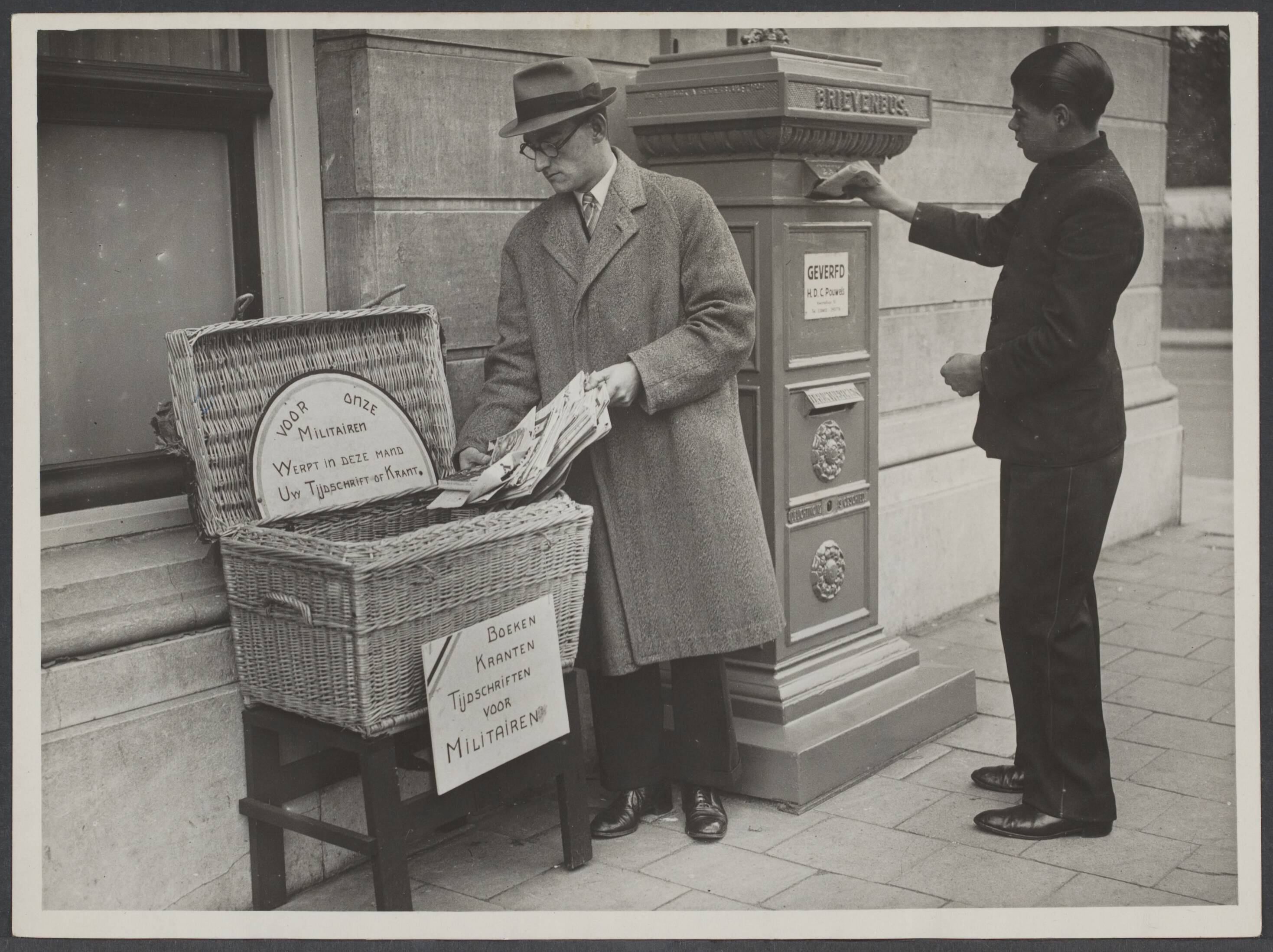 Steun aan de Nederlandse soldaat — Den Haag. Naast de brievenbus heeft de Ned. Ver. voor Vreemdelingenverkeer (V.V.V.) een mand geplaatst , waar men tijdschriften of boeken kan deponeren — Foto: N.V. Vereenigde Fotobureaux. Licentie: Set B: Rechtenvrij / Publiek Domein. Bron: Nationaal Archief. http://hdl.handle.net/10648/6ad911c1-9a65-c85d-a61e-11f0b6c411c1