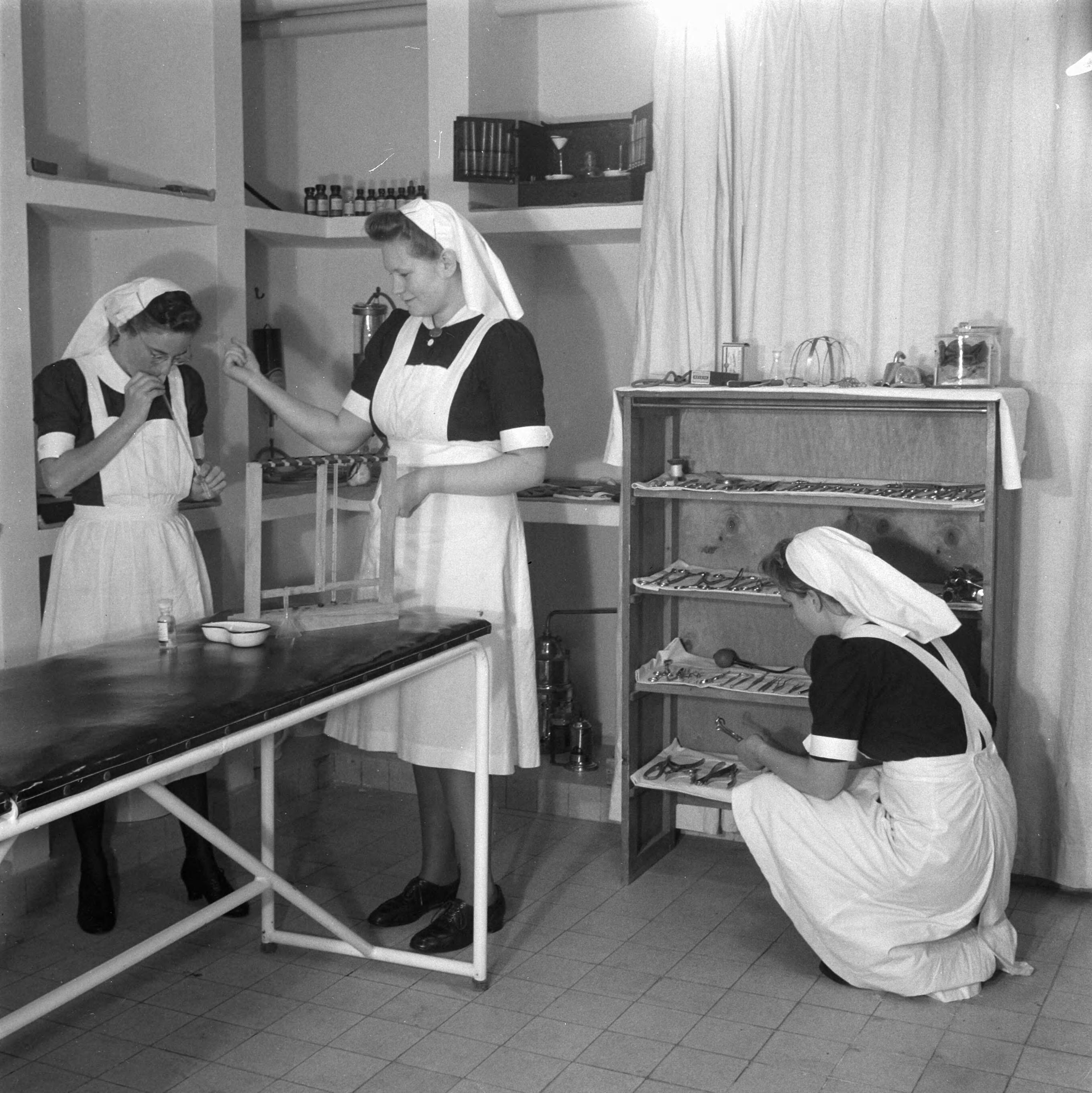 Verpleegstersschool — De eerste Katholieke Opleiding voor Verpleegkundigen in Park Vronesteyn in Voorburg. Drie verpleegkundigen zijn aan het werk in de operatiekamer — Foto: Wisman, Bram / Anefo. Licentie: Set B: Rechtenvrij / Publiek Domein. Bron: Nationaal Archief. http://hdl.handle.net/10648/a8ae45e2-d0b4-102d-bcf8-003048976d84