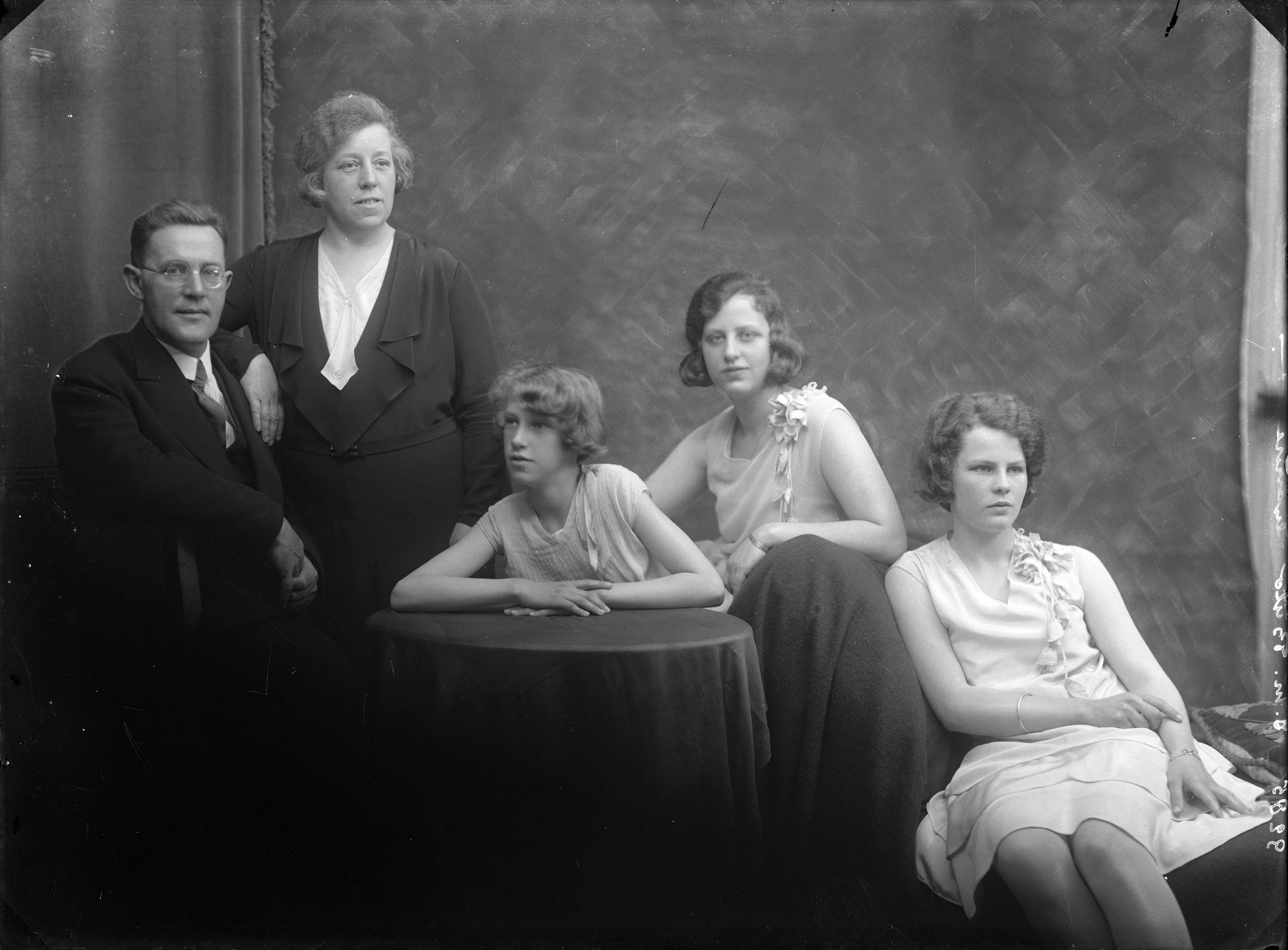 Portretten — Studio-opnames. Portret van een gezin. Vader, moeder en hun drie tienerdochters. De meisjes in witte jurken, de moeder in zwart-wit en vader in kostuum. Haarlem, Nederland. 1918-1930.9285 I.M. Bulo gravure — Foto: Berg, Th.C.J. van den / Spaarnestad Photo (05887). Licentie: Set B: Rechtenvrij / Publiek Domein. Bron: Nationaal Archief. http://hdl.handle.net/10648/35429da7-c7fe-a382-e063-6df0900a6686