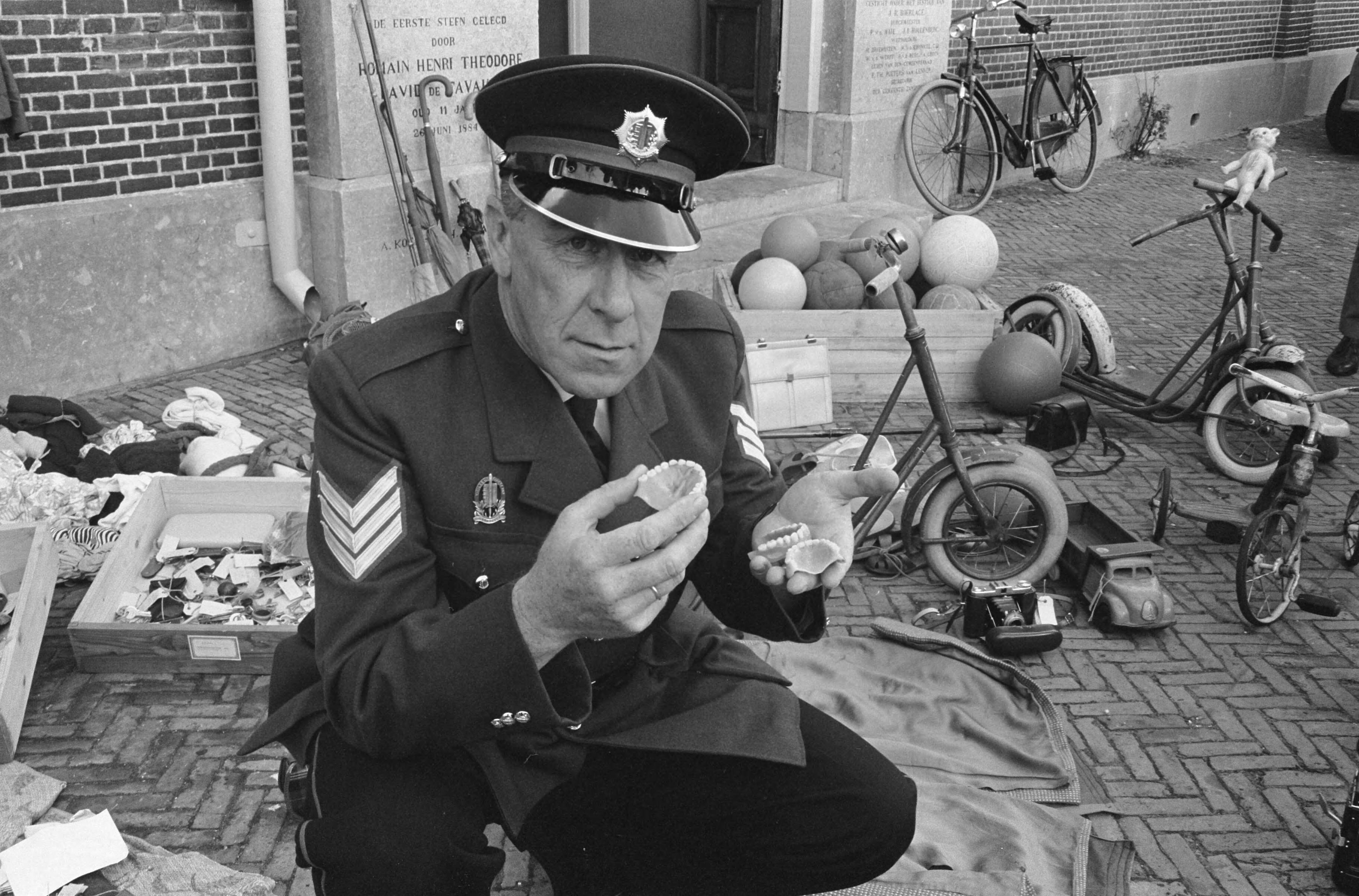 Fotocollectie Anefo — Einde zomerseizoen in Zandvoort. Politieagent sorteert de gevonden voorwerpen. In zijn handen kunstgebitten — Foto: Pot, Harry / Anefo. Licentie: Set B: Rechtenvrij / Publiek Domein. Bron: Nationaal Archief. http://hdl.handle.net/10648/a9e522aa-d0b4-102d-bcf8-003048976d84