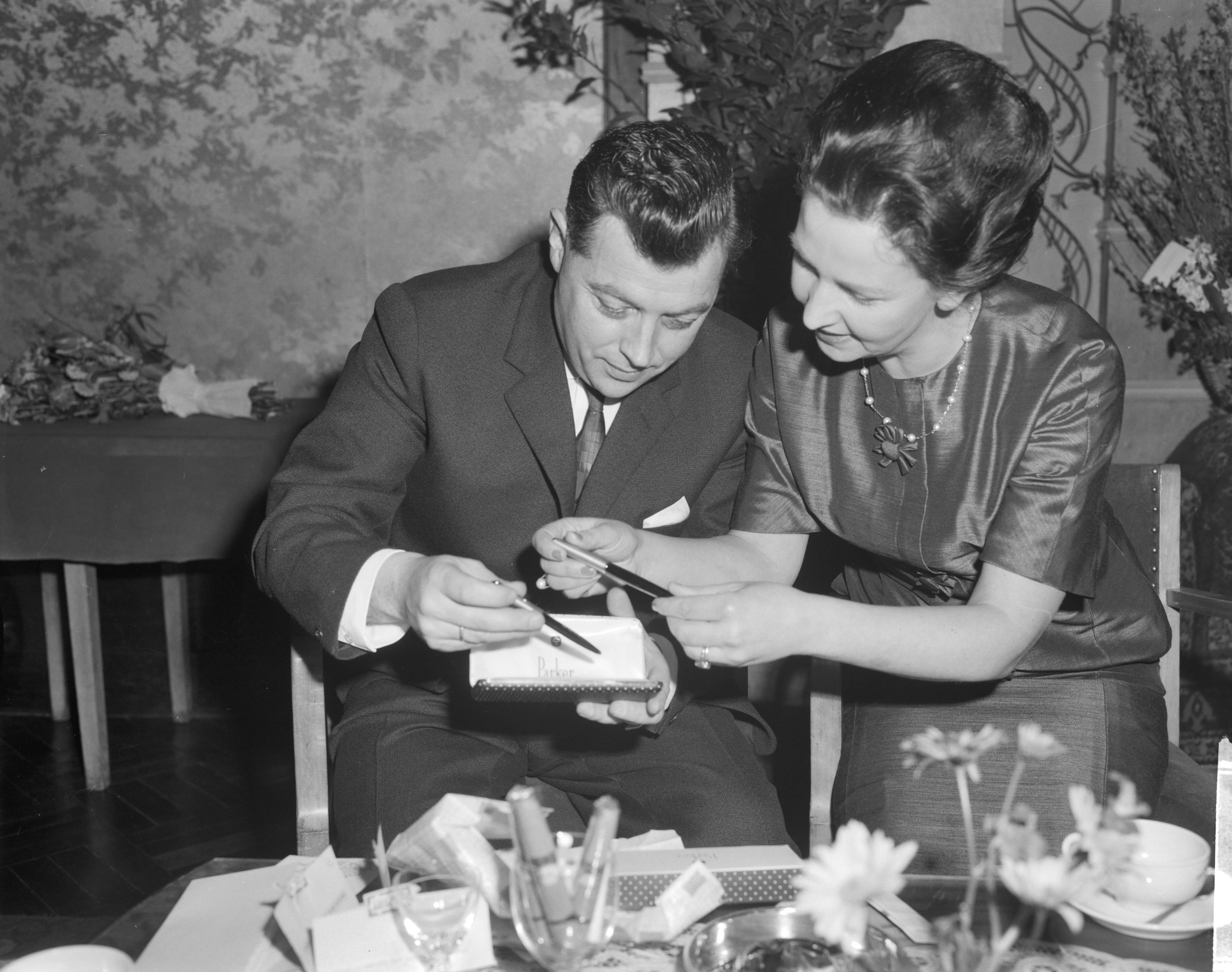 Fotocollectie Anefo — Carel Enkelaar heeft afscheid genomen als hoofd van het NTS-journaal in Hof van Holland te Hilversum, Carel Enkelaar en zijn vrouw bekijken geschenken (ballpennen) — Foto: Bilsen, Joop van / Anefo. Licentie: Set B: Rechtenvrij / Publiek Domein. Bron: Nationaal Archief. http://hdl.handle.net/10648/aa28417a-d0b4-102d-bcf8-003048976d84