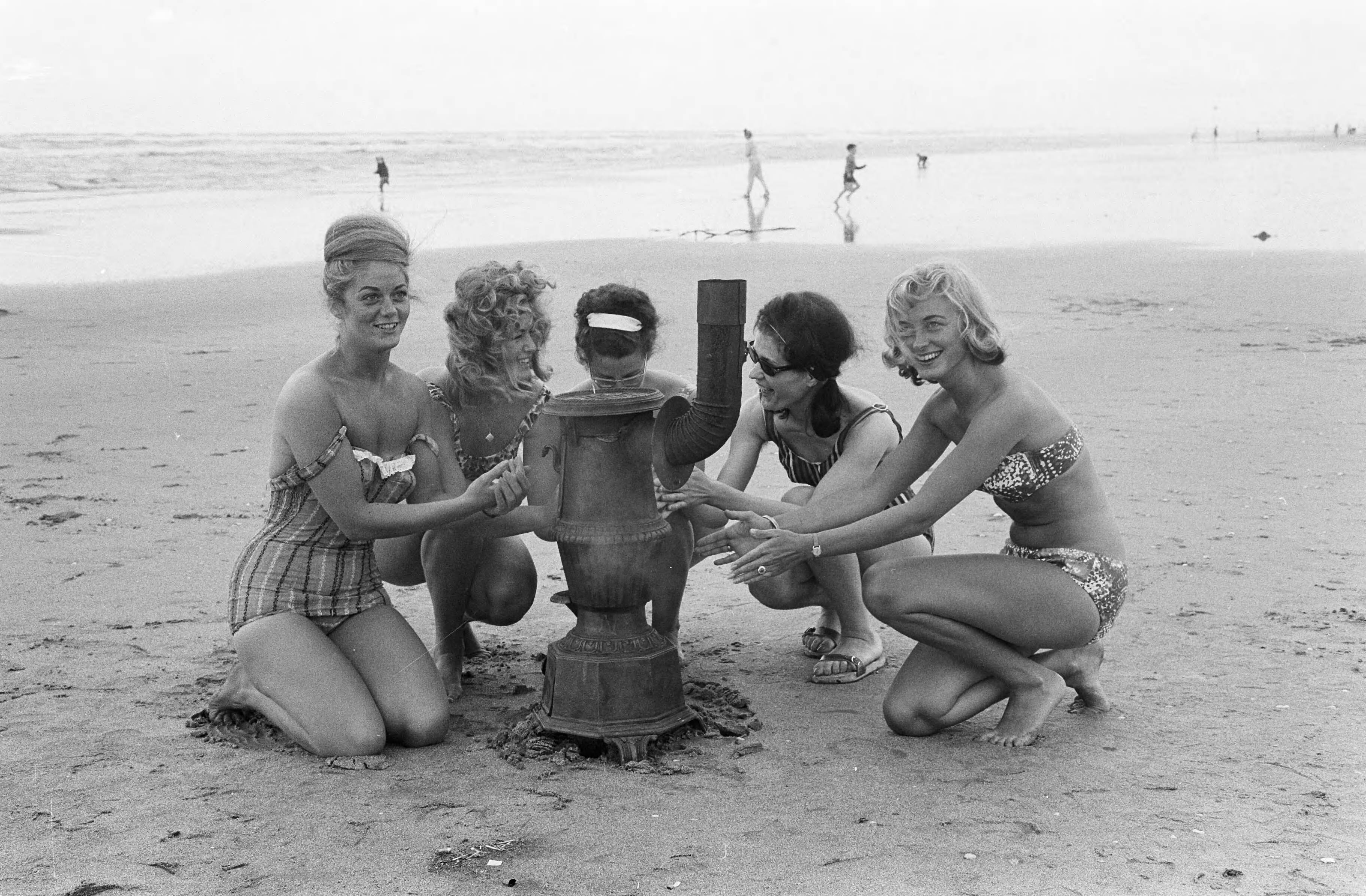 Fotocollectie Anefo — Slecht weer strand Zandvoort. Vijf vrouwelijke optimisten rond een kachel op het strand — Foto: Pot, Harry / Anefo. Licentie: Set B: Rechtenvrij / Publiek Domein. Bron: Nationaal Archief. http://hdl.handle.net/10648/aa0f6038-d0b4-102d-bcf8-003048976d84