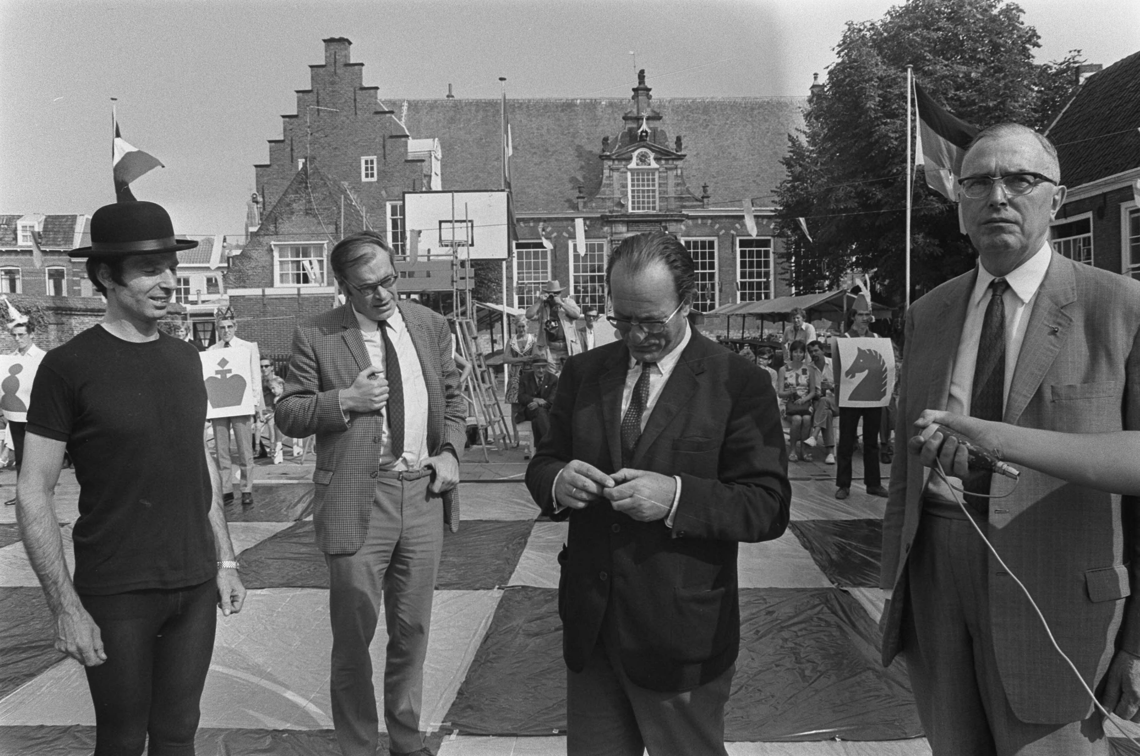 Fotocollectie Anefo — Godfried Bomans en dr. Max Euwe spelen schaakspel met levende stukken, Haarlem — Foto: Mieremet, Rob / Anefo. Licentie: Set B: Rechtenvrij / Publiek Domein. Bron: Nationaal Archief. http://hdl.handle.net/10648/aba12fee-d0b4-102d-bcf8-003048976d84