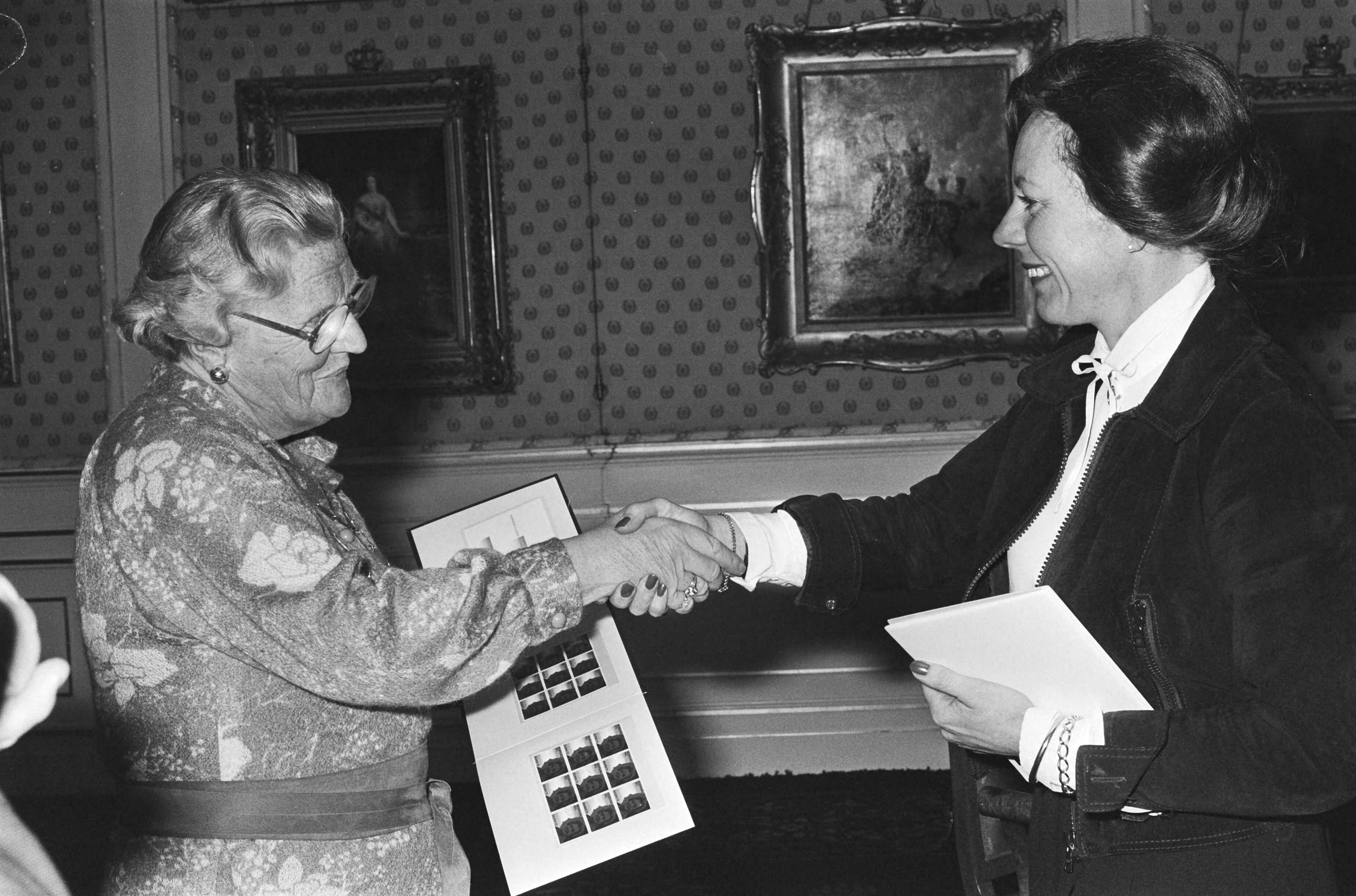 Postzegels ter gelegenheid van de 70ste verjaardag van Hare Majesteit door staatssecretaris Smit Kroes uitgereikt aan koningin Juliana op paleis Soestdijk — Smit-Kroes, Neelie|Juliana (koningin Nederland)|Soestdijk|koninginnen |postzegels |staatssecretarissen|Utrecht|Paleis Soestdijk — Foto: Suyk, Koen / Anefo. Licentie: Set B: Rechtenvrij / Publiek Domein. Bron: Nationaal Archief. http://hdl.handle.net/10648/acc6ba4c-d0b4-102d-bcf8-003048976d84
