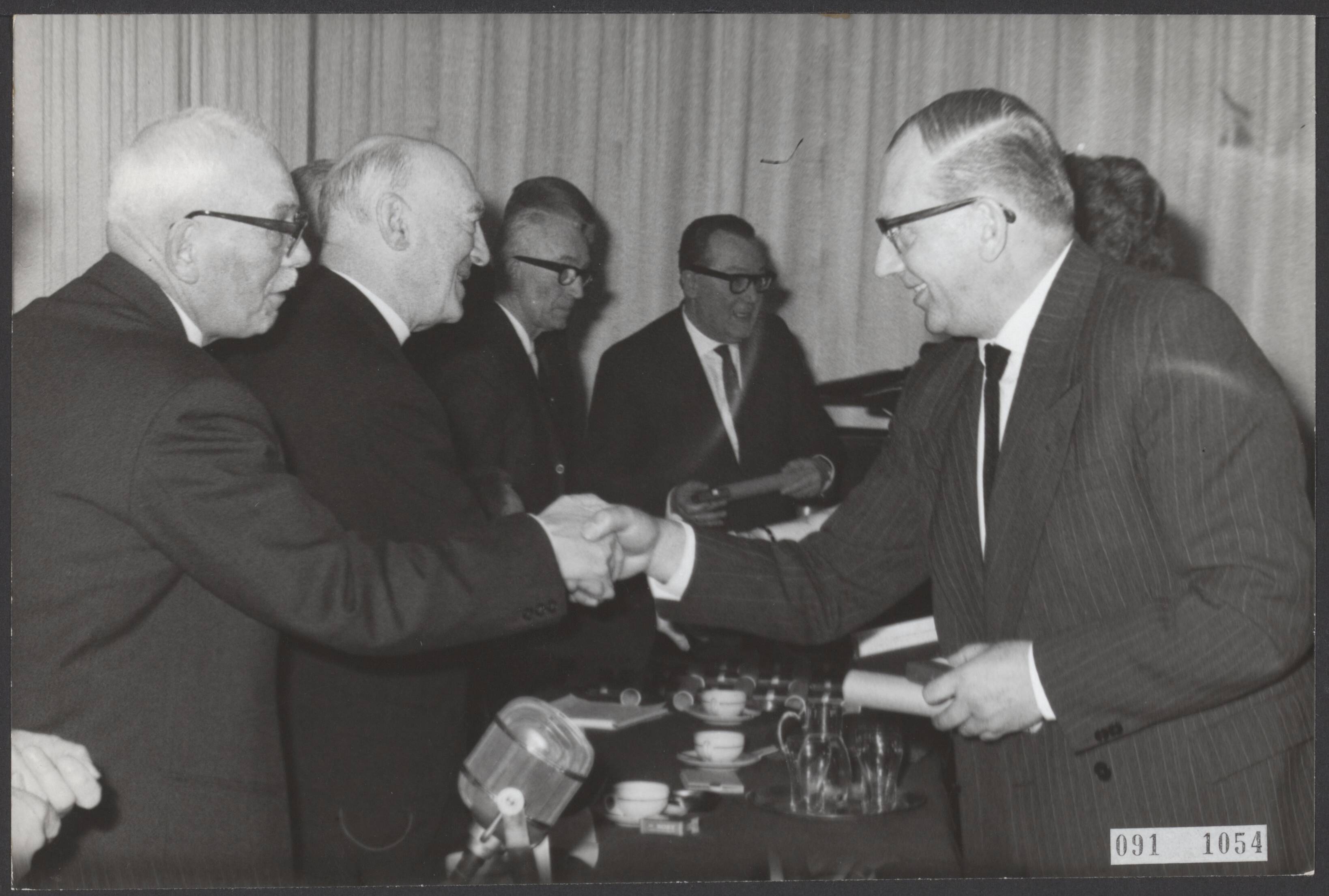 Fotocollectie Elsevier Binnenland — Huldiging in Hotel Gooiland te Hilversum, georganiseerd door de N.R.U. van 23 medewerkers op op of na 1 maart 1963 gedurende 25 werkzaam zijn bij NRU, NTS, AVRO, KRO en NCRV. De heer Everse die 25 jaar werkzaam is bij de KRO wordt gelukgewnest door de voorzitter van de Nederlandse Radio Unie, mr. A.B. Roosjen (links) — Foto: Gelderen, Hugo van / Anefo. Licentie: Set B: Rechtenvrij / Publiek Domein. Bron: Nationaal Archief. http://hdl.handle.net/10648/ae21cdbe-d0b4-102d-bcf8-003048976d84