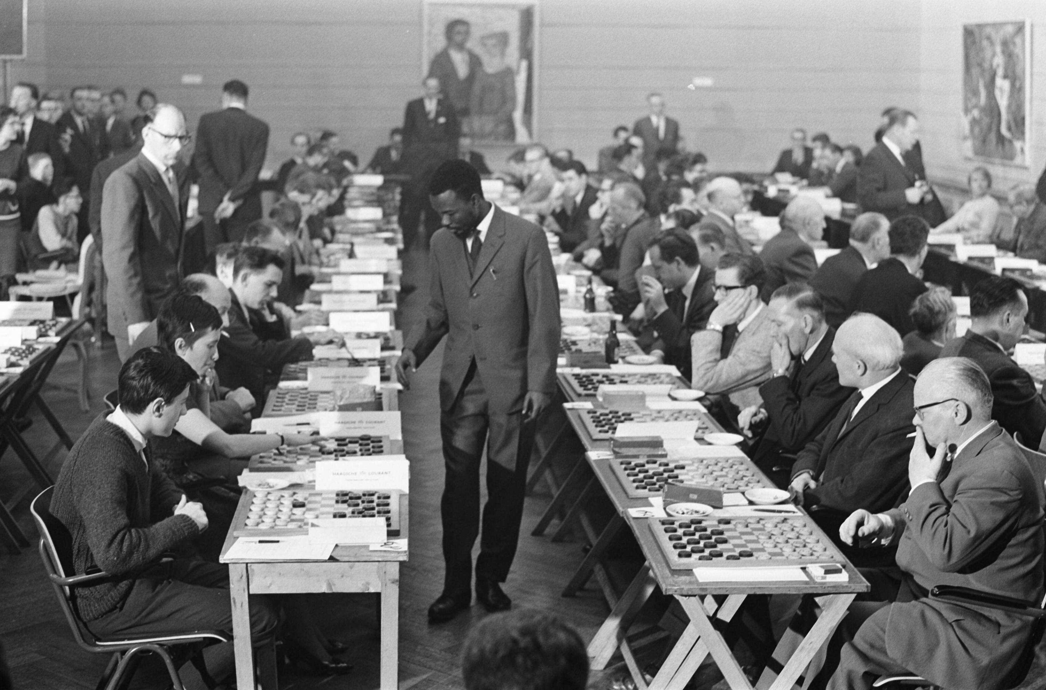 Fotocollectie Anefo — Wereldrecord simultaandammen van Baba Sy in Den Haag. Baba Sy tijdens de simultaanseance — Foto: Rossem, Wim van / Anefo. Licentie: Set B: Rechtenvrij / Publiek Domein. Bron: Nationaal Archief. http://hdl.handle.net/10648/a9f639f0-d0b4-102d-bcf8-003048976d84