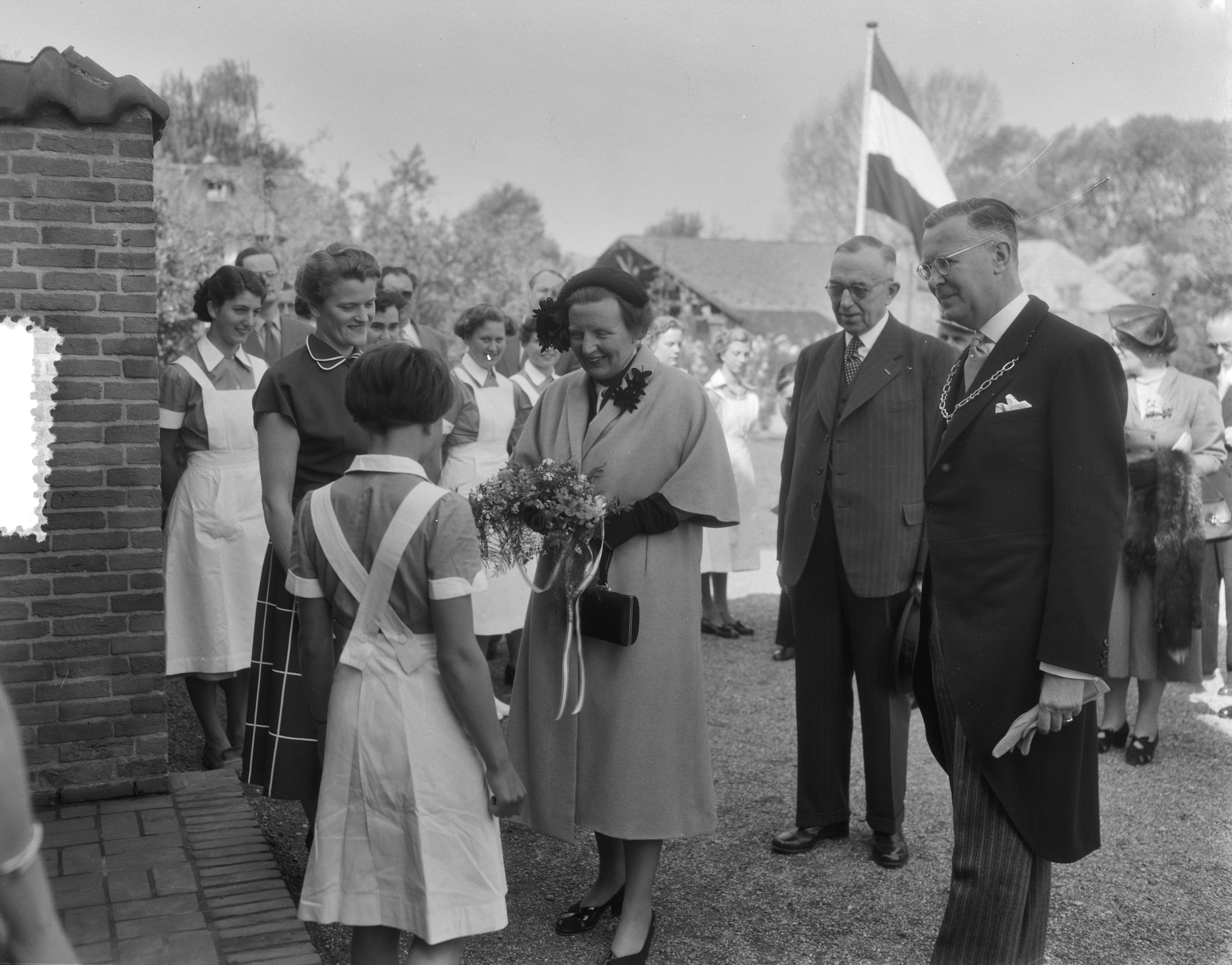 Werkbezoek van koningin Juliana aan de provincie Groningen (1954) — Werkbezoek van koningin Juliana aan de provincie Groningen, Bezoek aan de Theda Mansholtschool te Haren. Titi Koekkoek overhandigt de koningin bloemen bij aankomst. Rechts de burgemeester van Haren, mr. F.W. van Ketwich Verschuur, 2e van rechts Commissaris der Koningin E.H. Ebels en links de directrice van de school, mej. W.H. Redeker — Foto: Duinen, G.W. van / Anefo. Licentie: Set B: Rechtenvrij / Publiek Domein. Bron: Nationaal Archief. http://hdl.handle.net/10648/a9229302-d0b4-102d-bcf8-003048976d84
