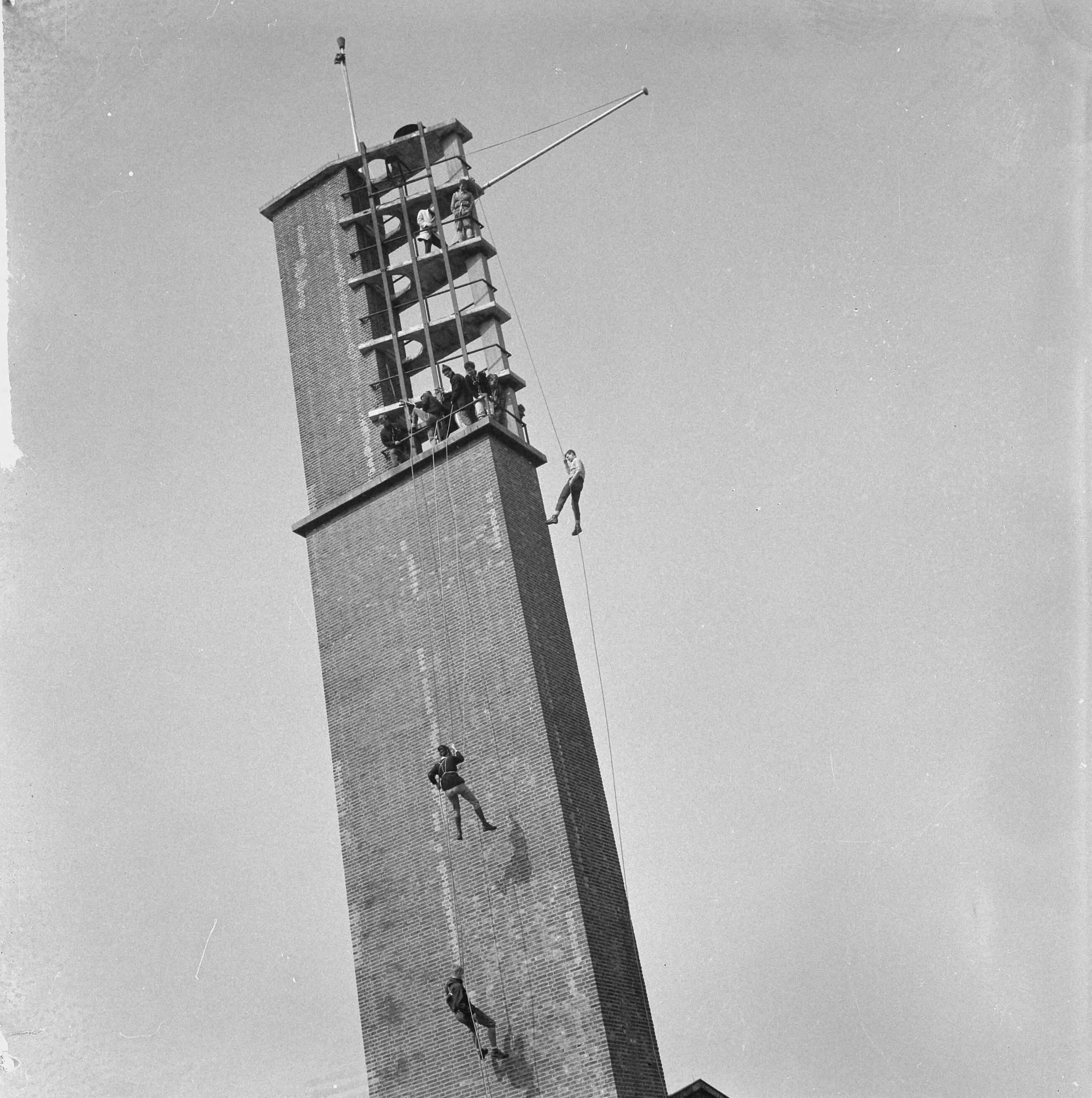 Fotocollectie Anefo — Kamp Houtrust 1965 geopend door wethouder mr. M. Vrolijk van Den Haag, leden van de Delftse Studenten Alpenclub tijdens het "abseilen" van de 32 meter hoge toren van de Houtrusthallen — Foto: Nijs, Jac. de / Anefo. Licentie: Set B: Rechtenvrij / Publiek Domein. Bron: Nationaal Archief. http://hdl.handle.net/10648/aa9ee5a0-d0b4-102d-bcf8-003048976d84