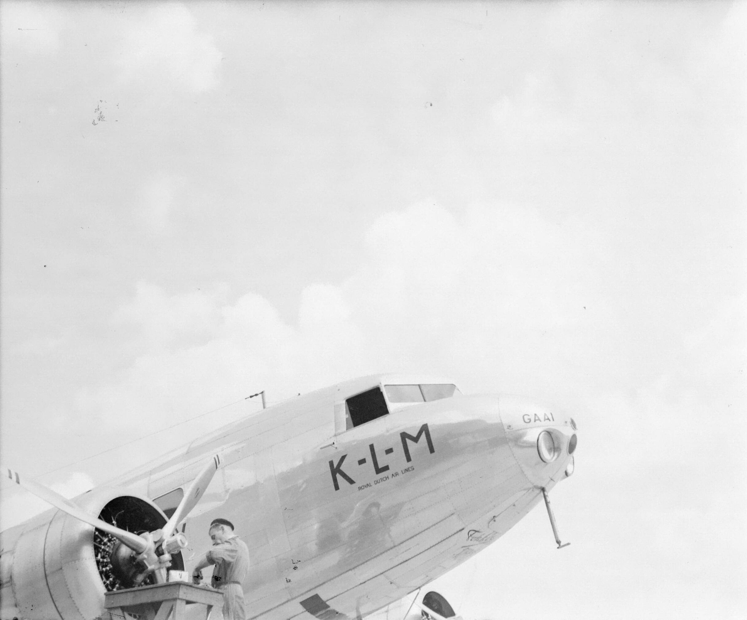 Reportage Schiphol — Een vliegtuigmonteur werkt aan de stuurboordmotor van de KLM Douglas DC-2 PH-AKG "Gaai" op luchthaven Schiphol — Foto: Poll, Willem van de. Licentie: Set B: Rechtenvrij / Publiek Domein. Bron: Nationaal Archief. http://hdl.handle.net/10648/aef230da-d0b4-102d-bcf8-003048976d84