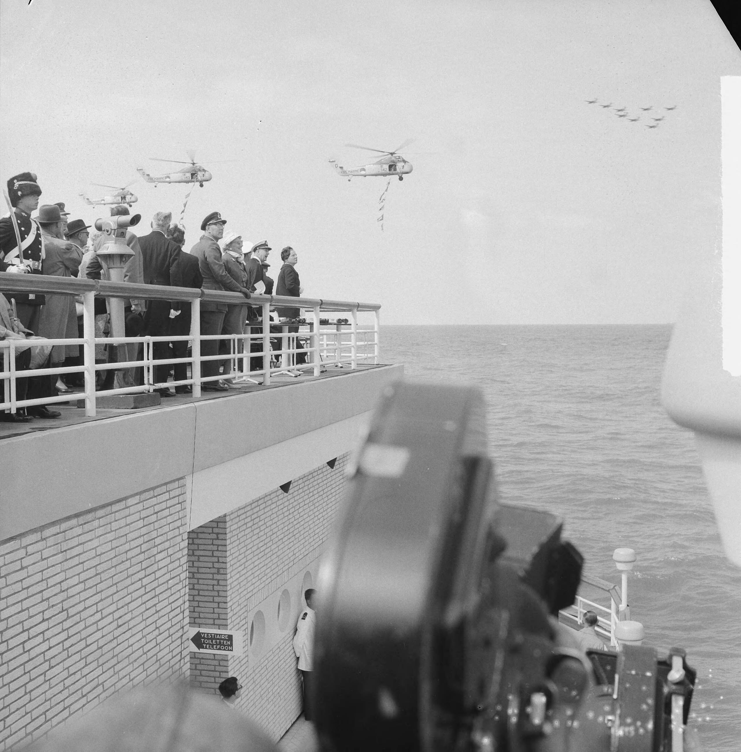 Fotocollectie Anefo — Vlootschouw Scheveningen. Koningin Juliana kijkt naar voorbijvliegende helicopters — Foto: Lindeboom, Henk / Anefo. Licentie: Set B: Rechtenvrij / Publiek Domein. Bron: Nationaal Archief. http://hdl.handle.net/10648/a9dbc82c-d0b4-102d-bcf8-003048976d84