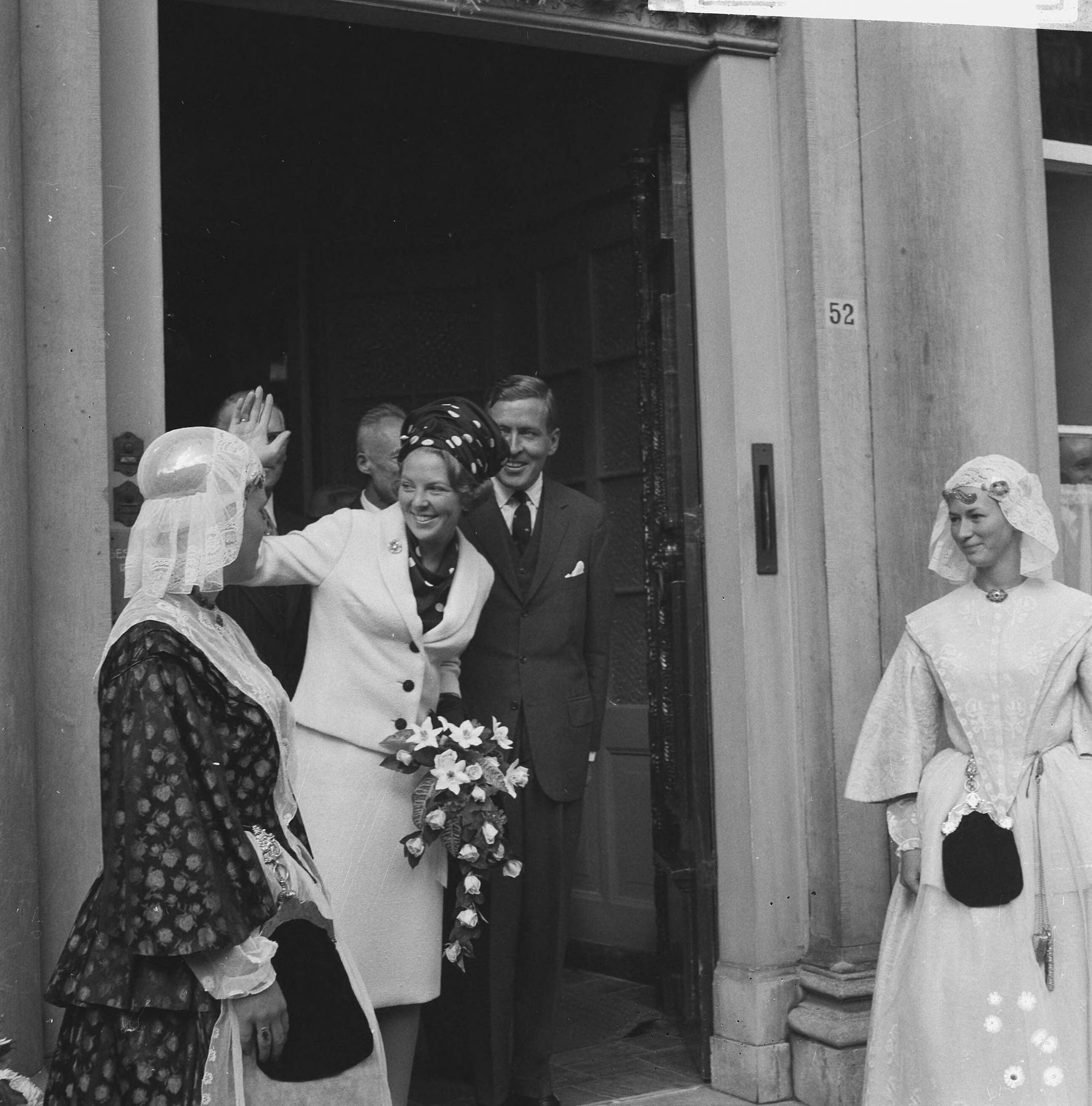 Bezoek van prinses Beatrix en Claus von Amsberg aan de drie noordelijke provincies — Bezoek prinses Beatrix en haar verloofde Claus von Amsberg aan Leeuwarden, zwaaiend in de ingang van het Provinciehuis. Aan weerszijden meisjes in Friese klederdracht — Foto: Kroon, Ron / Anefo. Licentie: Set B: Rechtenvrij / Publiek Domein. Bron: Nationaal Archief. http://hdl.handle.net/10648/aabf007e-d0b4-102d-bcf8-003048976d84
