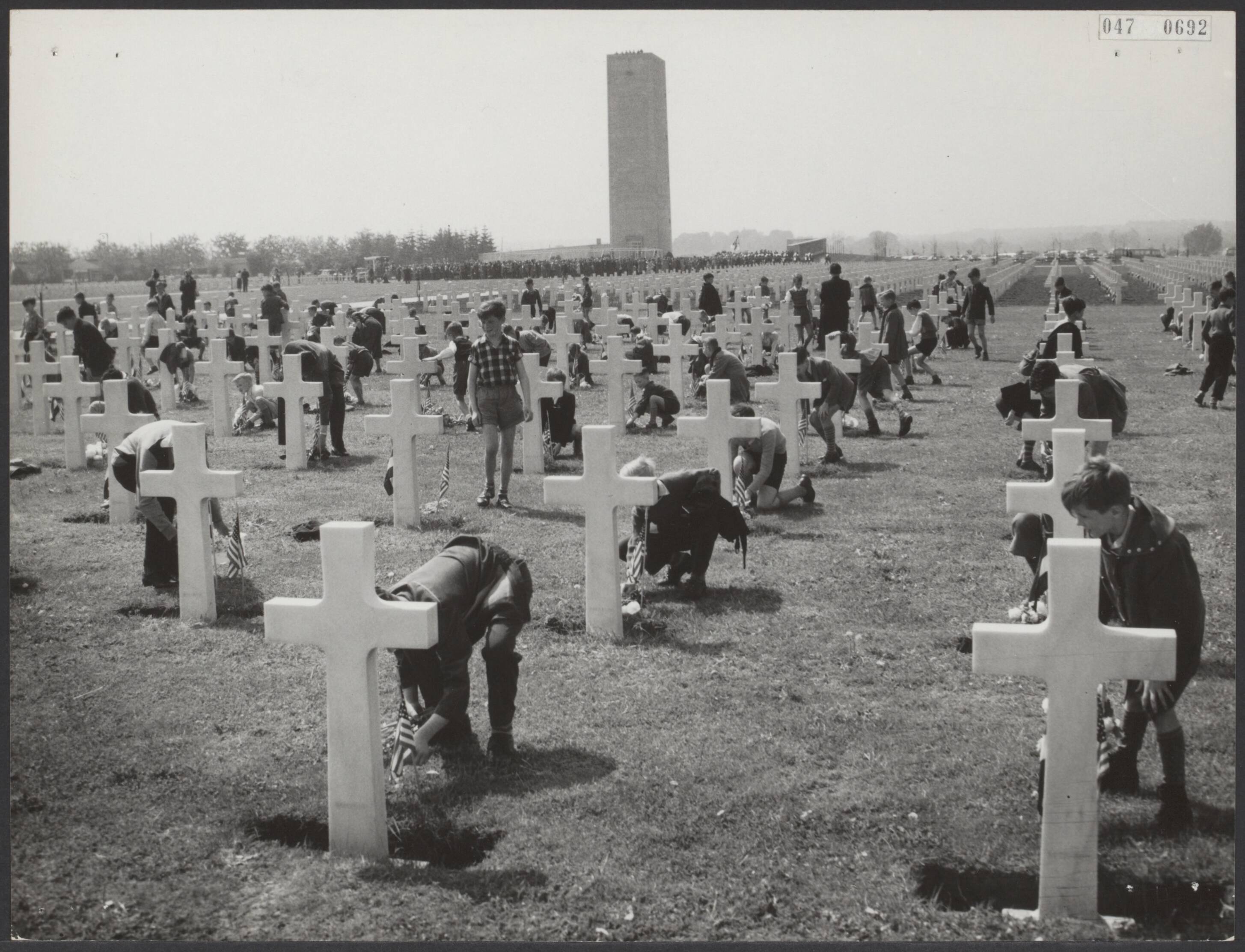 Fotocollectie Elsevier Binnenland — Memorial Day op het Amerikaanse soldatenkerkhof te Margraten in Zuid-Limburg. Hierbij waren aanwezig de Amerikaanse ambassadeur H. Freeman Matthews en de Commissaris der Konining in de provincie Limburg, dr. F.J.M. A. Houben. Door schoolkinderen werden bloemen op de graven gelegd, waarbij op de achtergrond het in aanbouw zijnde nieuwe monument — Foto: Noske, J.D. / Anefo. Licentie: Set B: Rechtenvrij / Publiek Domein. Bron: Nationaal Archief. http://hdl.handle.net/10648/ae001426-d0b4-102d-bcf8-003048976d84