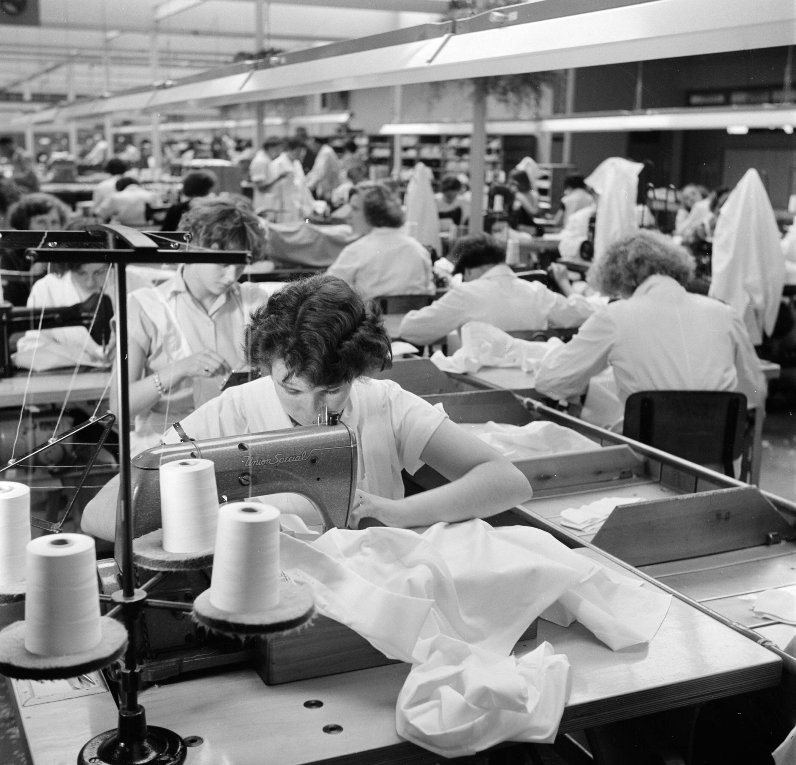 Reportage Kerko Haarlem — Zaal met naaisters aan naaimachine bij overhemdenbedrijf Kerko — Foto: Poll, Willem van de. Licentie: Set B: Rechtenvrij / Publiek Domein. Bron: Nationaal Archief. http://hdl.handle.net/10648/aecbc486-d0b4-102d-bcf8-003048976d84