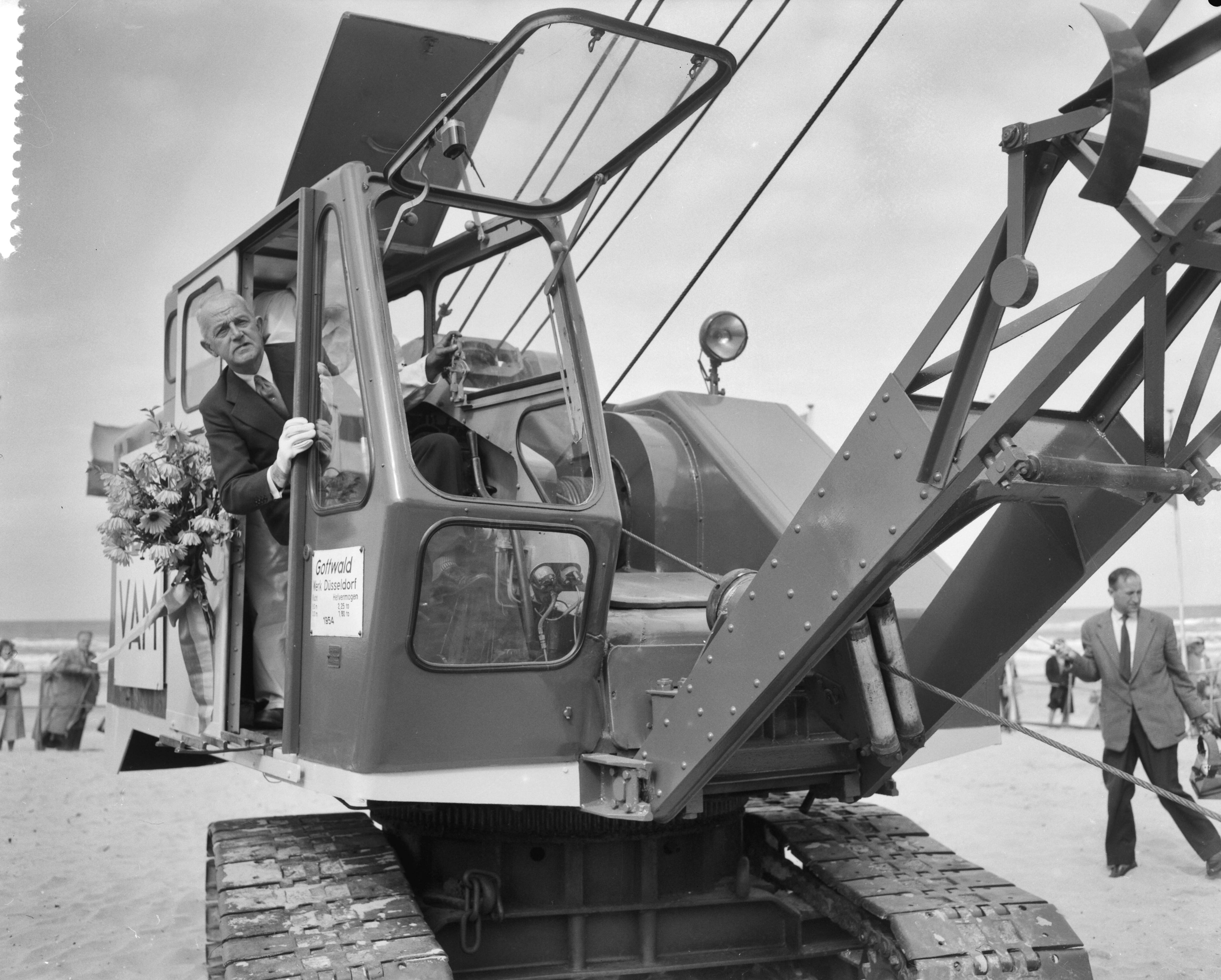 Fotocollectie Anefo — Burgemeester van Den Haag H.A.M.T. Kolfschoten geeft startsein voor de bouw van de nieuwe pier te Scheveningen, burgemeester Kolfschoten in de draglline — Foto: Behrens, Herbert F. / Anefo. Licentie: Set B: Rechtenvrij / Publiek Domein. Bron: Nationaal Archief. http://hdl.handle.net/10648/a99dbf32-d0b4-102d-bcf8-003048976d84
