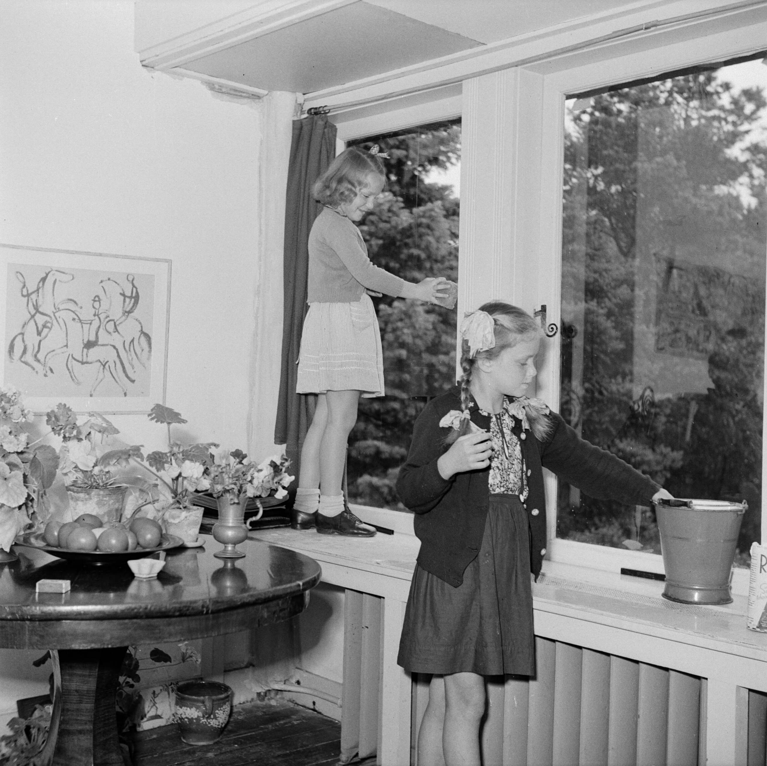Prinses Beatrix en prinses Irene op de Werkplaats Kindergemeenschap van Kees Boeke te Bilthoven — Prinses Irene poetst, staande op de vensterbank, een raam met een klasgenote — Foto: Poll, Willem van de. Licentie: Set B: Rechtenvrij / Publiek Domein. Bron: Nationaal Archief. http://hdl.handle.net/10648/aee8209a-d0b4-102d-bcf8-003048976d84