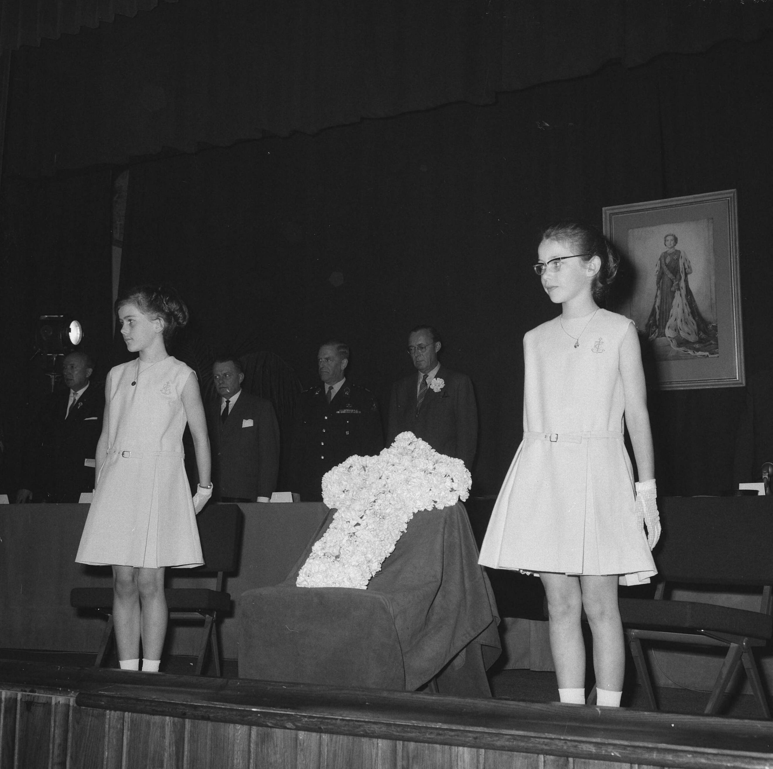 Fotocollectie Anefo — Bevrijdingscongres Nationale Federatie Raad van het Voormalig Verzet Nederland in de KMA te Breda, bijgewoond door prins Bernhard. Herdenking bij aanvang, twee meisjes plaatsen een kruis van witte anjers op een verhoging op het toneel — Foto: Nijs, Jac. de / Anefo. Licentie: Set B: Rechtenvrij / Publiek Domein. Bron: Nationaal Archief. http://hdl.handle.net/10648/aaa5c78a-d0b4-102d-bcf8-003048976d84