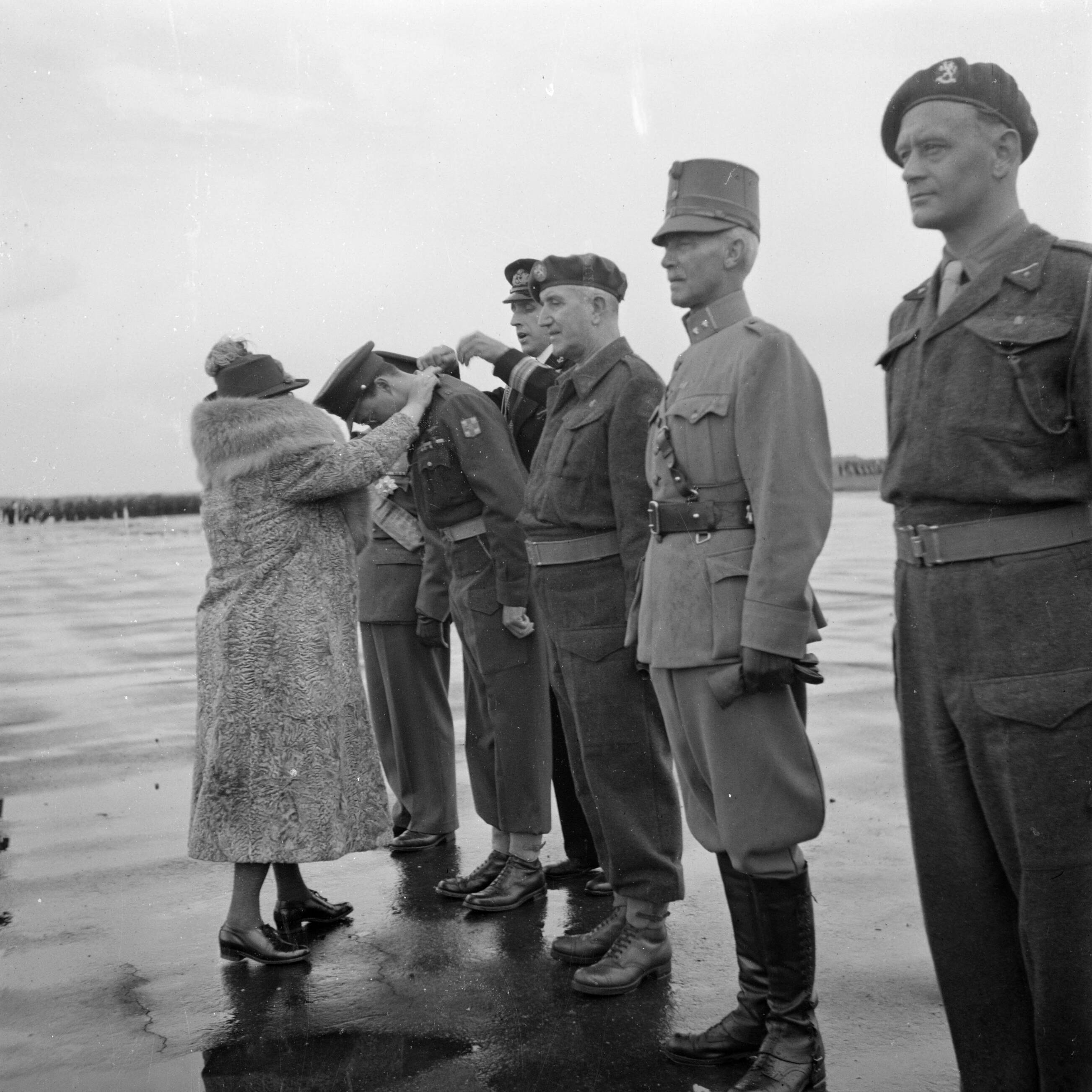 Uitreiking van de Militaire Willems-Orde en andere onderscheidingen door koningin Wilhelmina in aanwezigheid van de overige leden van de koninklijke familie op de vliegbasis Soesterberg — Koningin Wilhelmina reikt de versierselen van de Militaire Willems-Orde uit aan prins Bernhard. Tweede van rechts kolonel W.F. Hennink, commandant van de Grebbeberglinie in mei 1940 — Foto: Poll, Willem van de. Licentie: Set B: Rechtenvrij / Publiek Domein. Bron: Nationaal Archief. http://hdl.handle.net/10648/aee8edea-d0b4-102d-bcf8-003048976d84