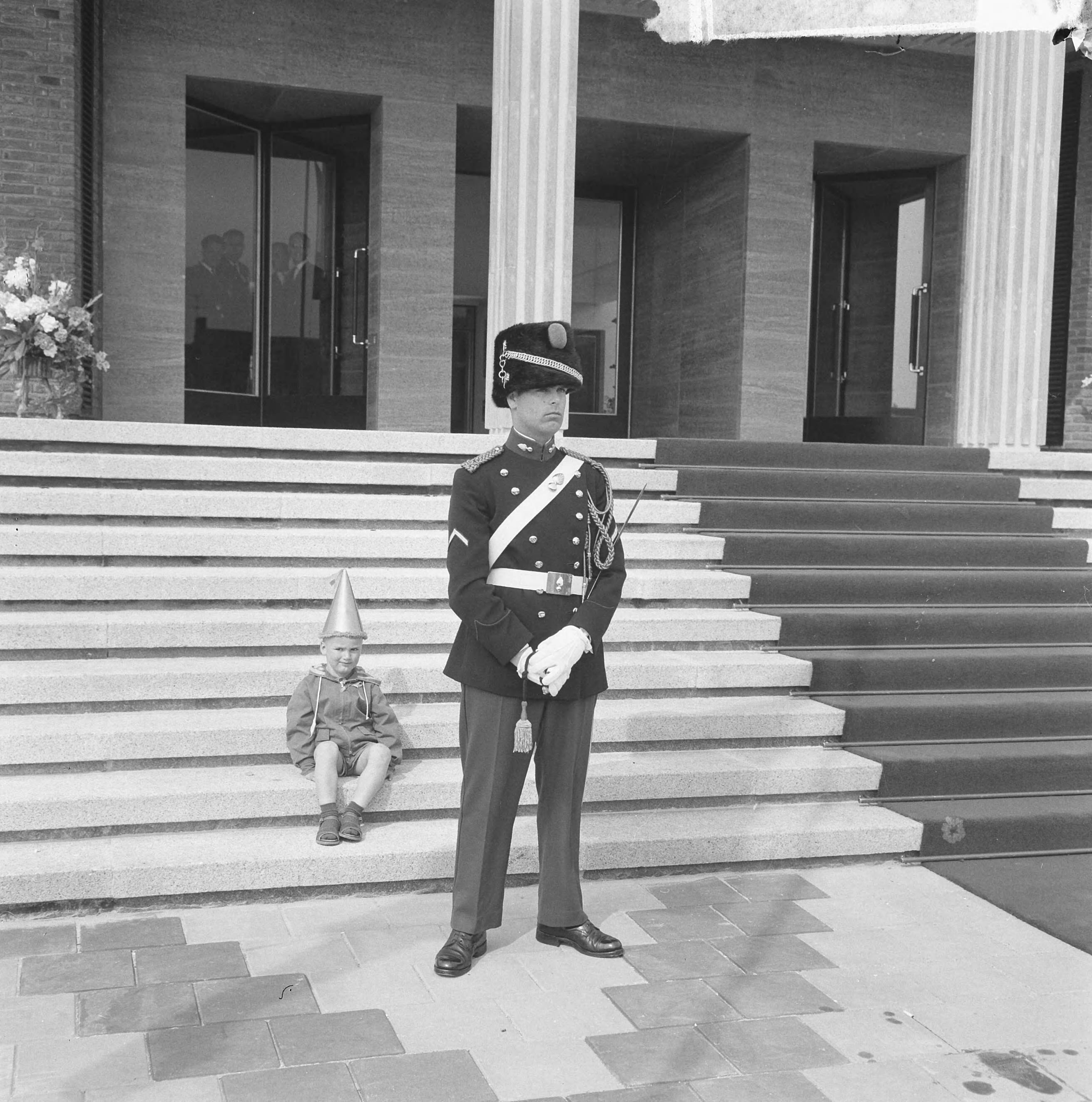 Koningin Juliana opent het nieuwe stadhuis te Vlissingen — Een jongetje met feestmuts zit op de trappen van het bordes van het stadhuis. Voor hem staat een marechaussee — Foto: Nijs, Jac. de / Anefo. Licentie: Set B: Rechtenvrij / Publiek Domein. Bron: Nationaal Archief. http://hdl.handle.net/10648/422ab3e9-36da-c86b-4164-89d9b8de16c7