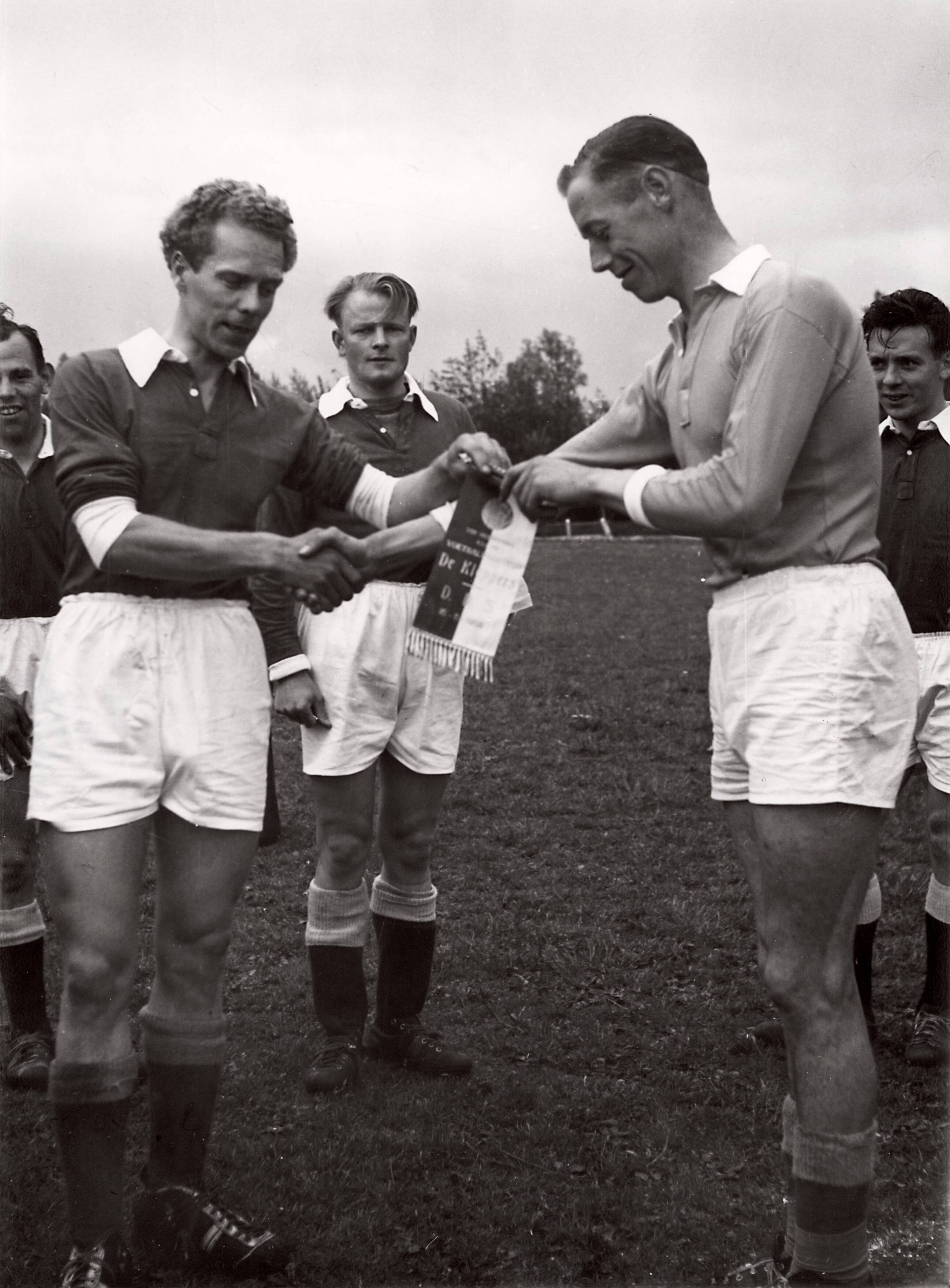 Sportactiviteiten personeel Drukkerij N.V. De Spaarnestad / Voetbal, o.a. F.C. Panorama — [Serie bedrijfsvoetbal Spaarnestad] Voetballers Spaarnestad [Serie bedrijfsvoetbal Spaarnestad] [uitwisselen van vaantje voor de wedstrijd, op het vaantje staat "De Kleppers" en "D.D.S." (motto Spaarnestad) en een datum] — Foto: Fotograaf Onbekend / Spaarnestad / Spaarnestad Photo (05887). Licentie: Set B: Rechtenvrij / Publiek Domein. Bron: Nationaal Archief. http://hdl.handle.net/10648/35429da6-3f17-a382-e063-6df0900a6686
