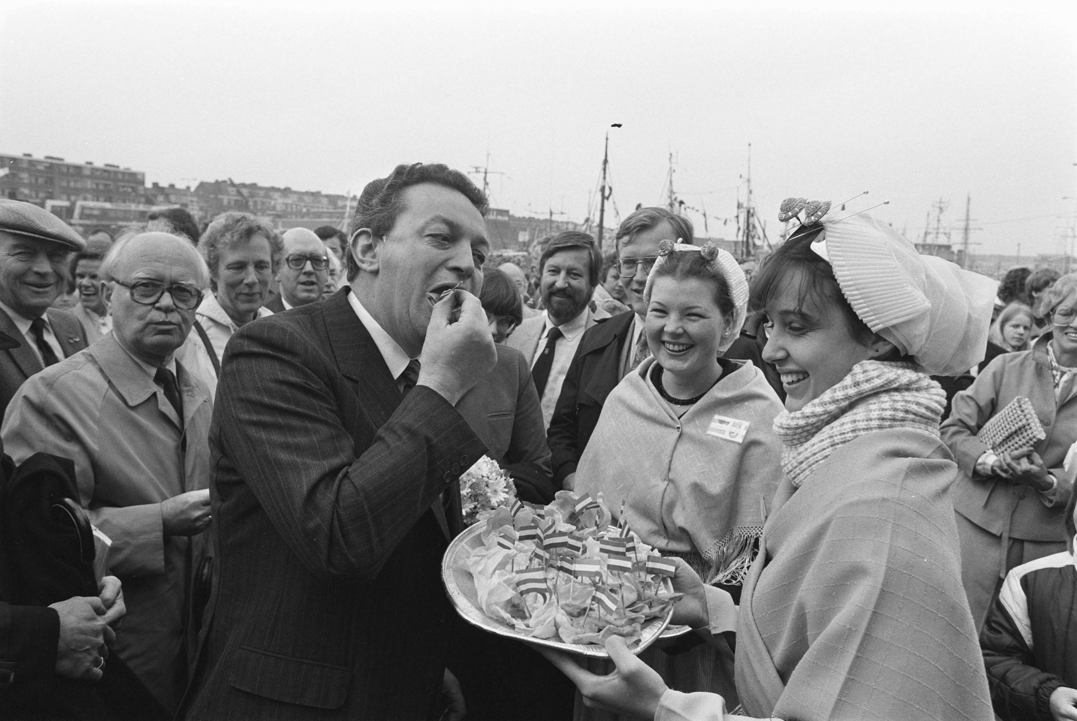 Vlaggetjesdag in Scheveningen 1983 — Minister Braks (Landbouw en Visserij) krijgt haring aangeboden door vrouwen in Scheveningse klederdracht — Foto: Croes, Rob C. / Anefo. Licentie: Set B: Rechtenvrij / Publiek Domein. Bron: Nationaal Archief. http://hdl.handle.net/10648/ad29d97e-d0b4-102d-bcf8-003048976d84