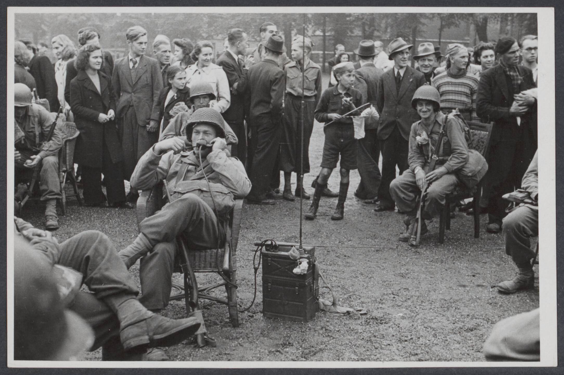 Nederland front, 1944 — Maastricht. Een Amerikaanse militair maakt het zich op het Vrijthof gemakkelijk en telefoneert, gezeten in een rieten stoel met de veldtelefoon — Foto: R.K. Foto-persbureau "Het Zuiden" / Rechtenvrij. Licentie: Set B: Rechtenvrij / Publiek Domein. Bron: Nationaal Archief. http://hdl.handle.net/10648/64c09e32-95be-edd7-4fe7-a93560c7d2b8