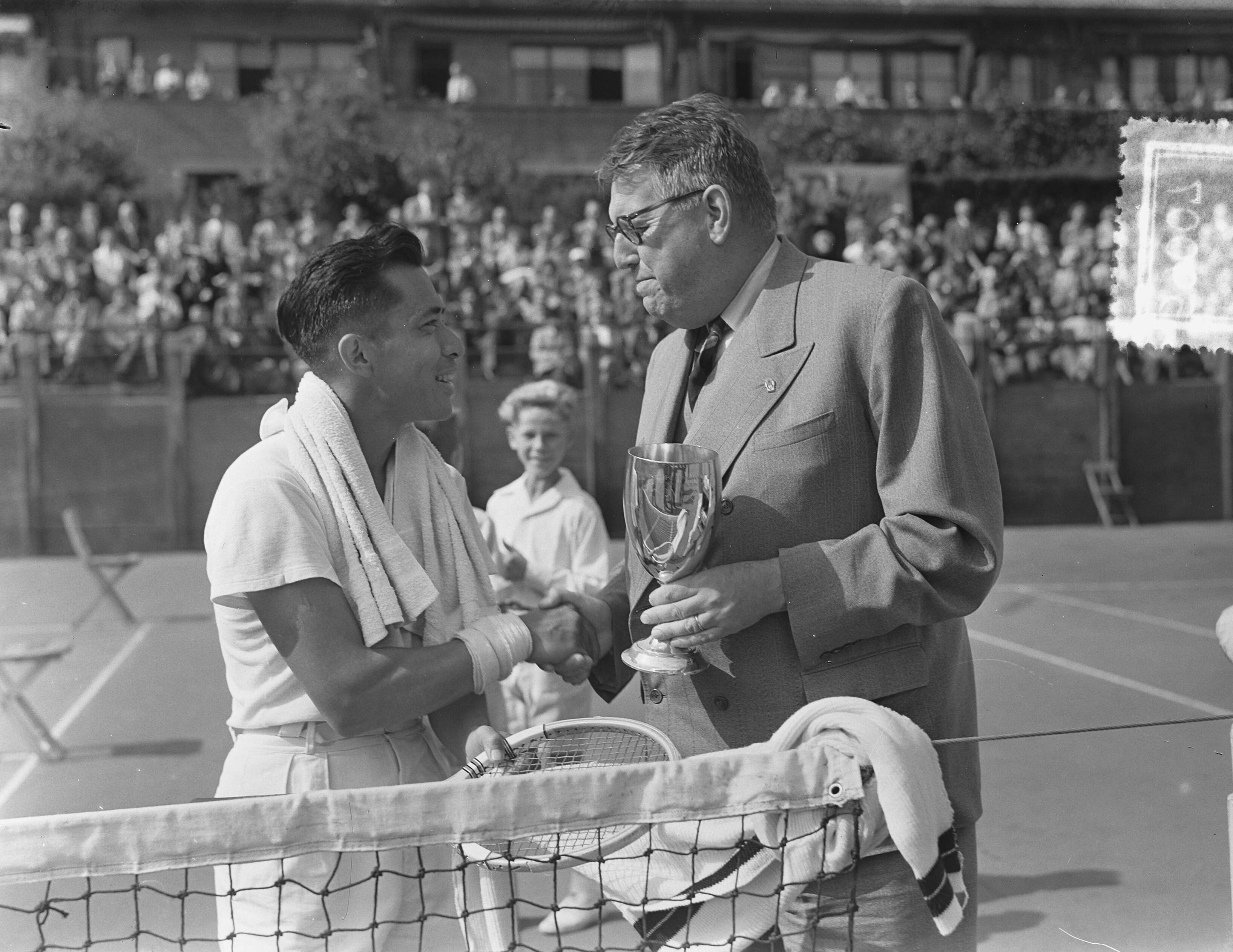 Tenniskampioenschappen Scheveningen — Tenniskampioenschappen Scheveningen. Lex Karamoy (links) won de titel in het enkelspel. Uitreiking van de beker door de vice-voorzitter van de K.N.L.B. mr. F. Meyer — Foto: Bilsen, Joop van / Anefo. Licentie: Set B: Rechtenvrij / Publiek Domein. Bron: Nationaal Archief. http://hdl.handle.net/10648/a9119a3e-d0b4-102d-bcf8-003048976d84