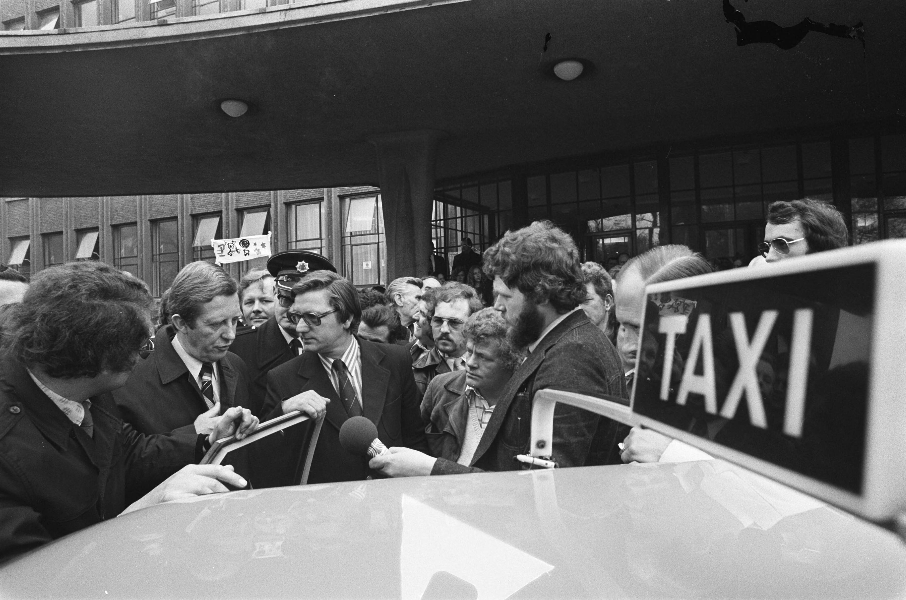 Demonstratie van taxichauffeurs in Den Haag en aanbieding van handtekeningen aan minister Tjerk Westerterp — Minister Tjerk Westerterp bekijkt een 'veilige' taxi — Foto: Mieremet, Rob / Anefo. Licentie: Set B: Rechtenvrij / Publiek Domein. Bron: Nationaal Archief. http://hdl.handle.net/10648/ac674986-d0b4-102d-bcf8-003048976d84