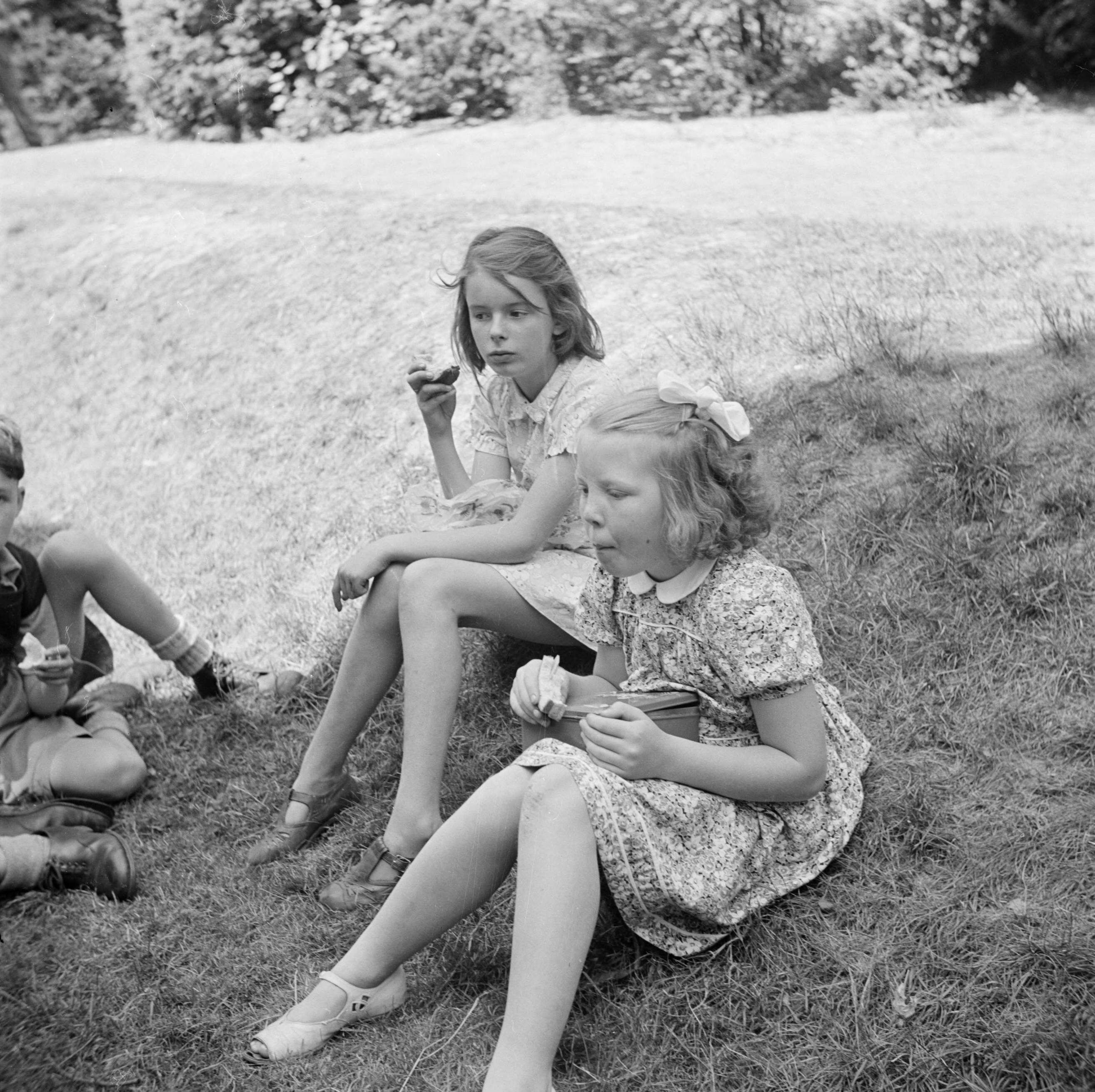 Prinses Beatrix en prinses Irene op de Werkplaats Kindergemeenschap van Kees Boeke te Bilthoven — Prinses Beatrix men een andere leerlinge eten boterhammen in de tuin — Foto: Poll, Willem van de. Licentie: Set B: Rechtenvrij / Publiek Domein. Bron: Nationaal Archief. http://hdl.handle.net/10648/aee80e84-d0b4-102d-bcf8-003048976d84