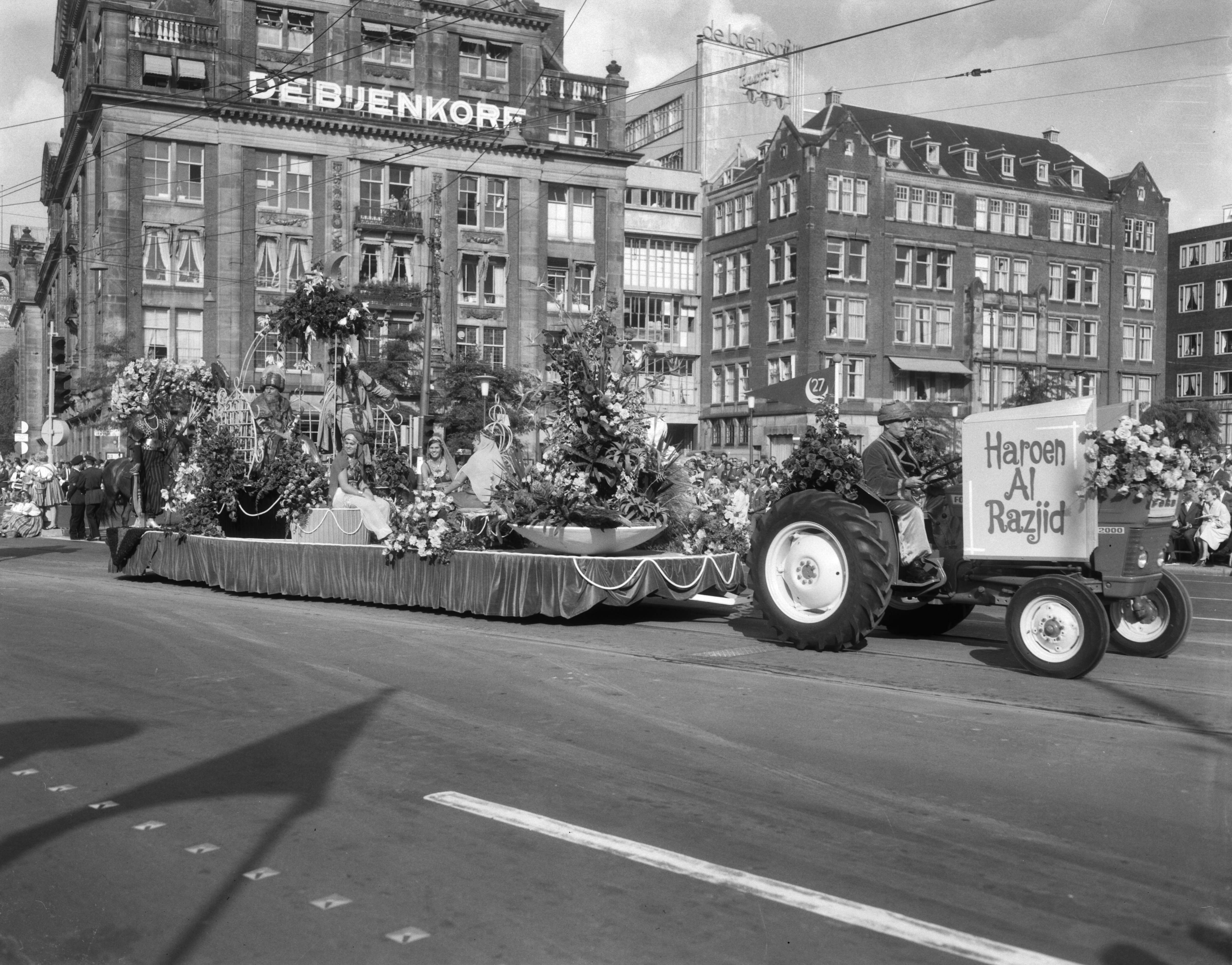 Bloemencorso van Aalsmeer te Amsterdam — Een praalwagen bij de Dam te Amsterdam met op de achtergrond het warenhuis de Bijenkorf — Foto: Bilsen, Joop van / Anefo. Licentie: Set B: Rechtenvrij / Publiek Domein. Bron: Nationaal Archief. http://hdl.handle.net/10648/aafaf21e-d0b4-102d-bcf8-003048976d84