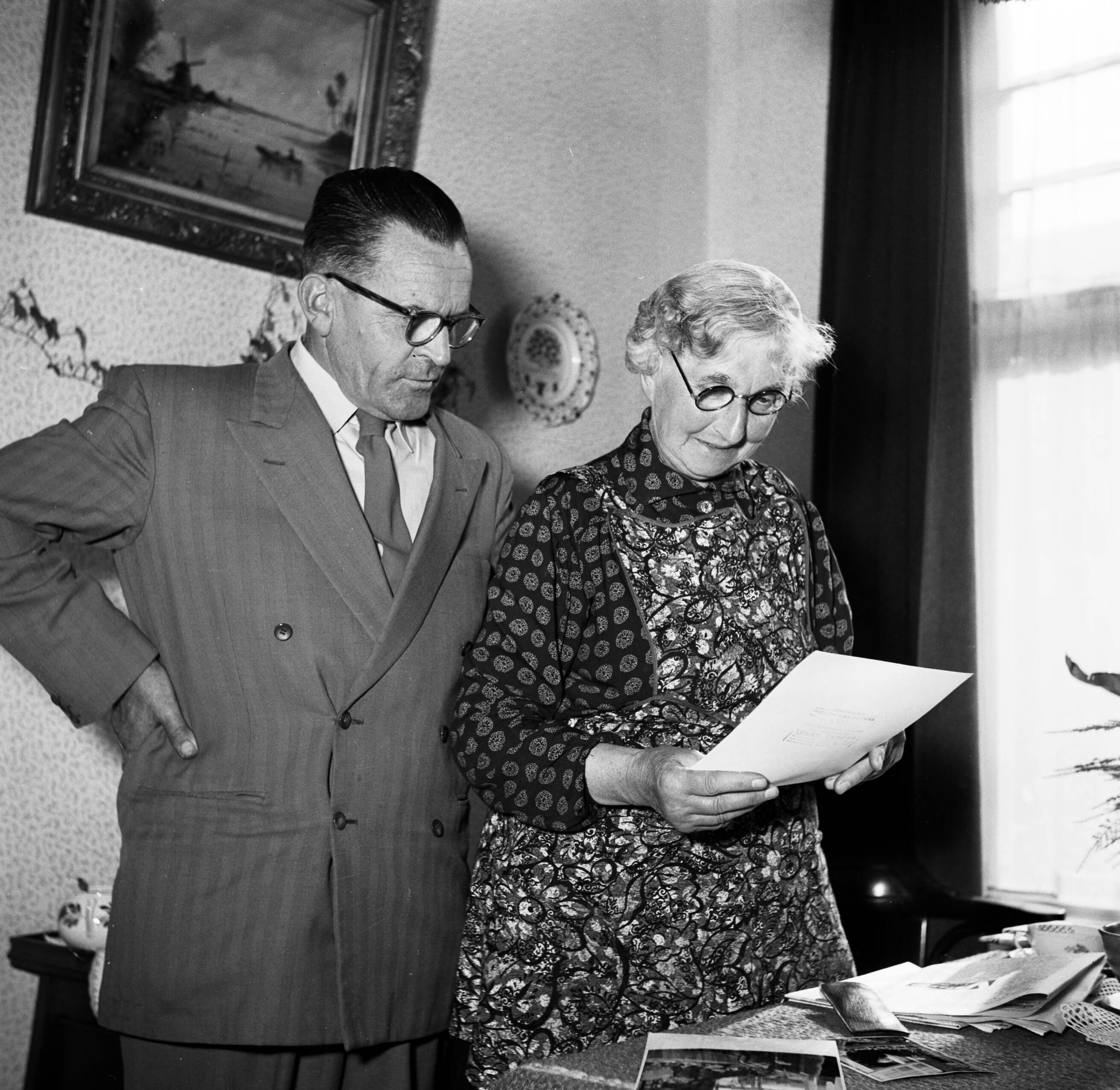 Fotocollectie Van de Poll — Gerard de Jongs moeder bestudert een brief terwijl Ynse Postma toekijkt — Foto: Poll, Willem van de. Licentie: Set B: Rechtenvrij / Publiek Domein. Bron: Nationaal Archief. http://hdl.handle.net/10648/aecce8b6-d0b4-102d-bcf8-003048976d84