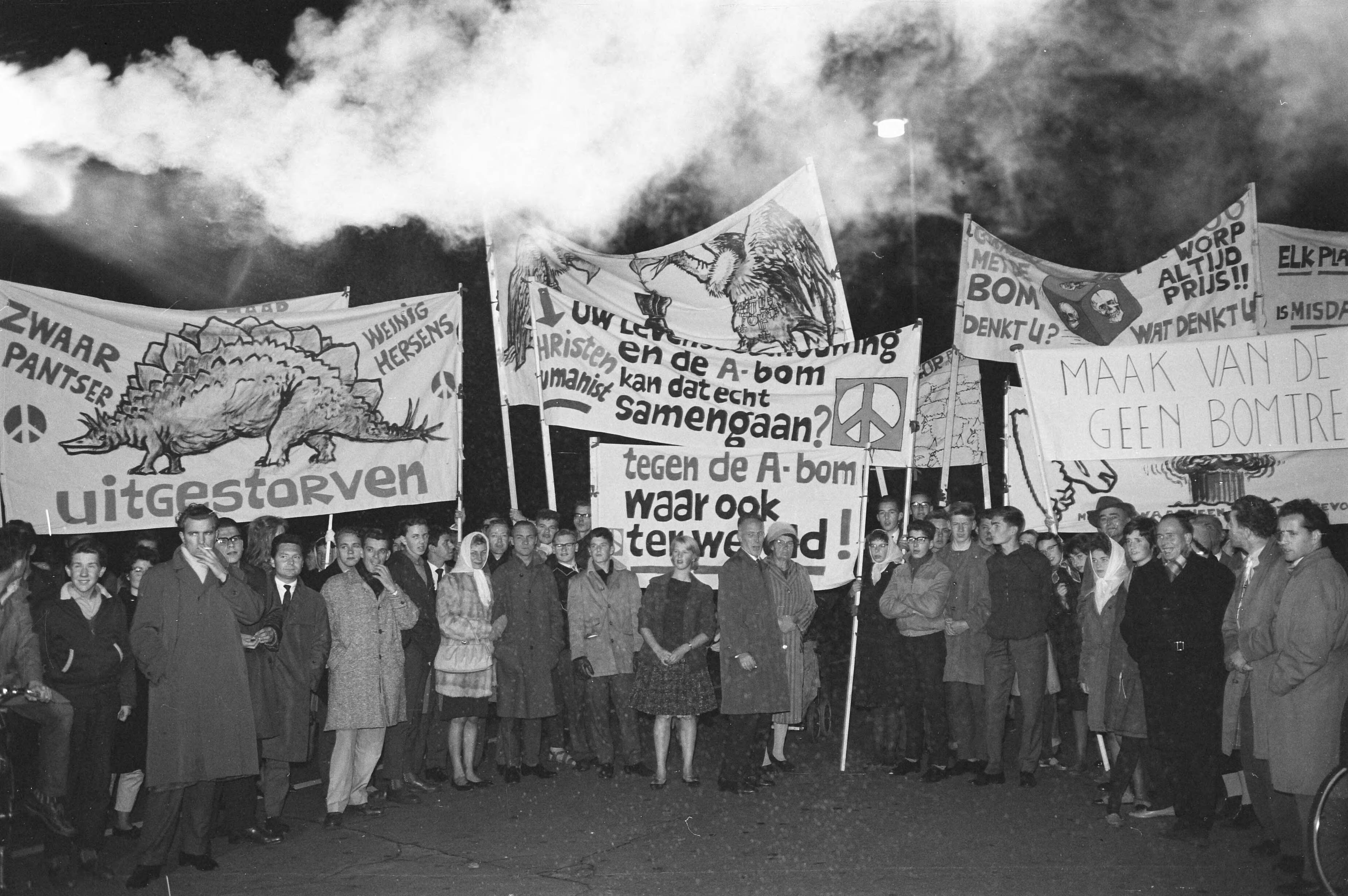 Fotocollectie Anefo — Betogers met spandoeken tijdens een anti-atoombomdemonstratie in Den Haag — Foto: Boer, […] de / Anefo. Licentie: Set B: Rechtenvrij / Publiek Domein. Bron: Nationaal Archief. http://hdl.handle.net/10648/a9e99718-d0b4-102d-bcf8-003048976d84