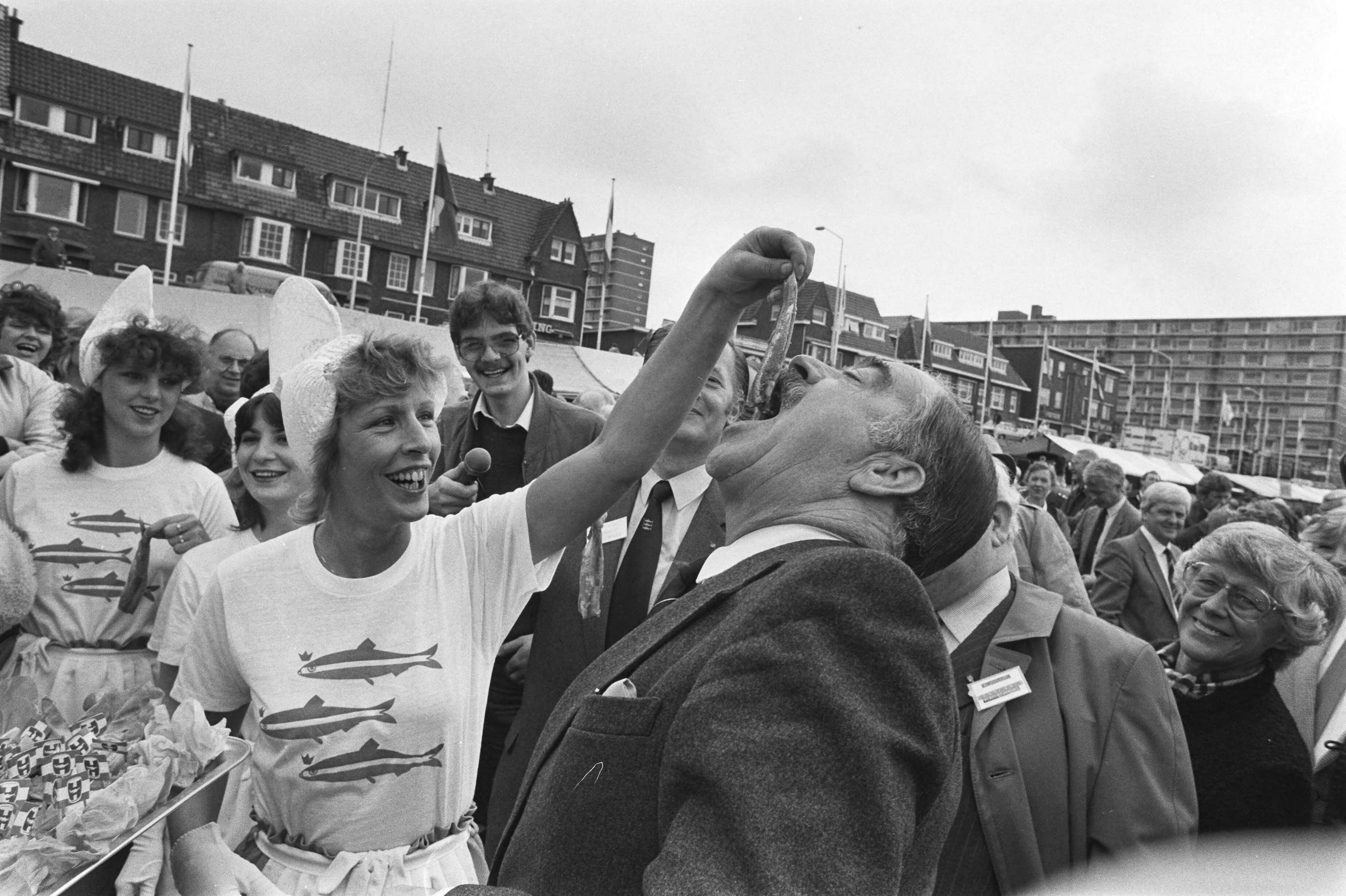 Fotocollectie Anefo — Vlaggetjesdag in Scheveningen; een "haringmeisje" voert staatssecretaris Ploeg een haring — Foto: Bogaerts, Rob / Anefo. Licentie: Set B: Rechtenvrij / Publiek Domein. Bron: Nationaal Archief. http://hdl.handle.net/10648/ad394116-d0b4-102d-bcf8-003048976d84