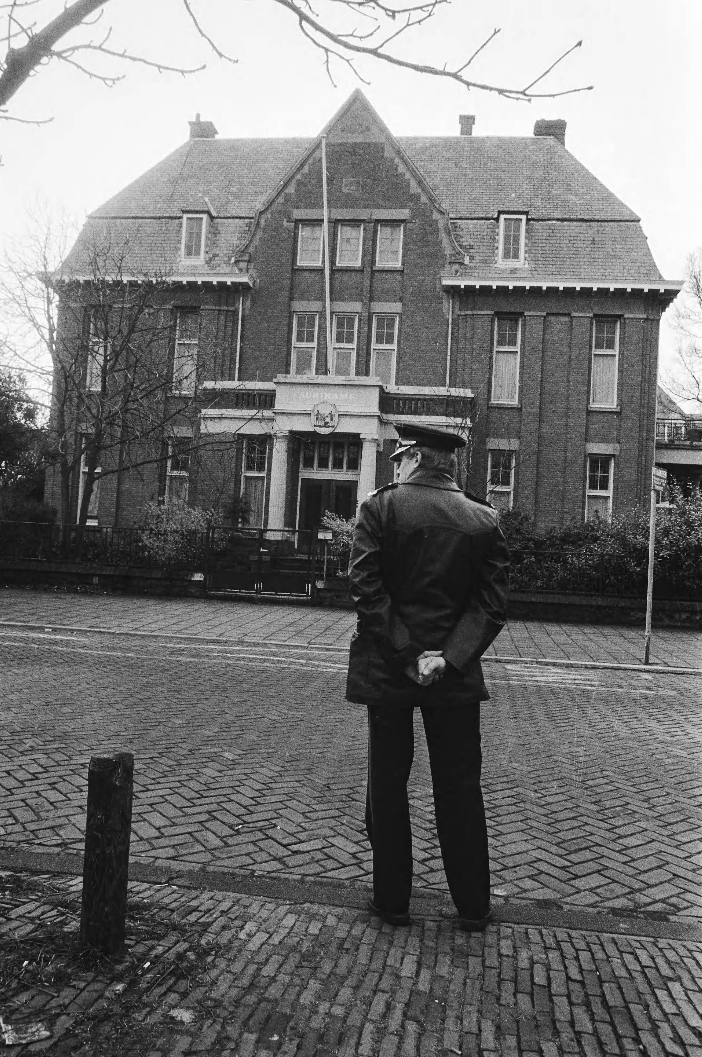 Surinaamse ambassade in Den Haag verlaten na bedreiging — Surinaamse ambassade met agent ervoor — Foto: Bogaerts, Rob / Anefo. Licentie: Set B: Rechtenvrij / Publiek Domein. Bron: Nationaal Archief. http://hdl.handle.net/10648/ad22f500-d0b4-102d-bcf8-003048976d84
