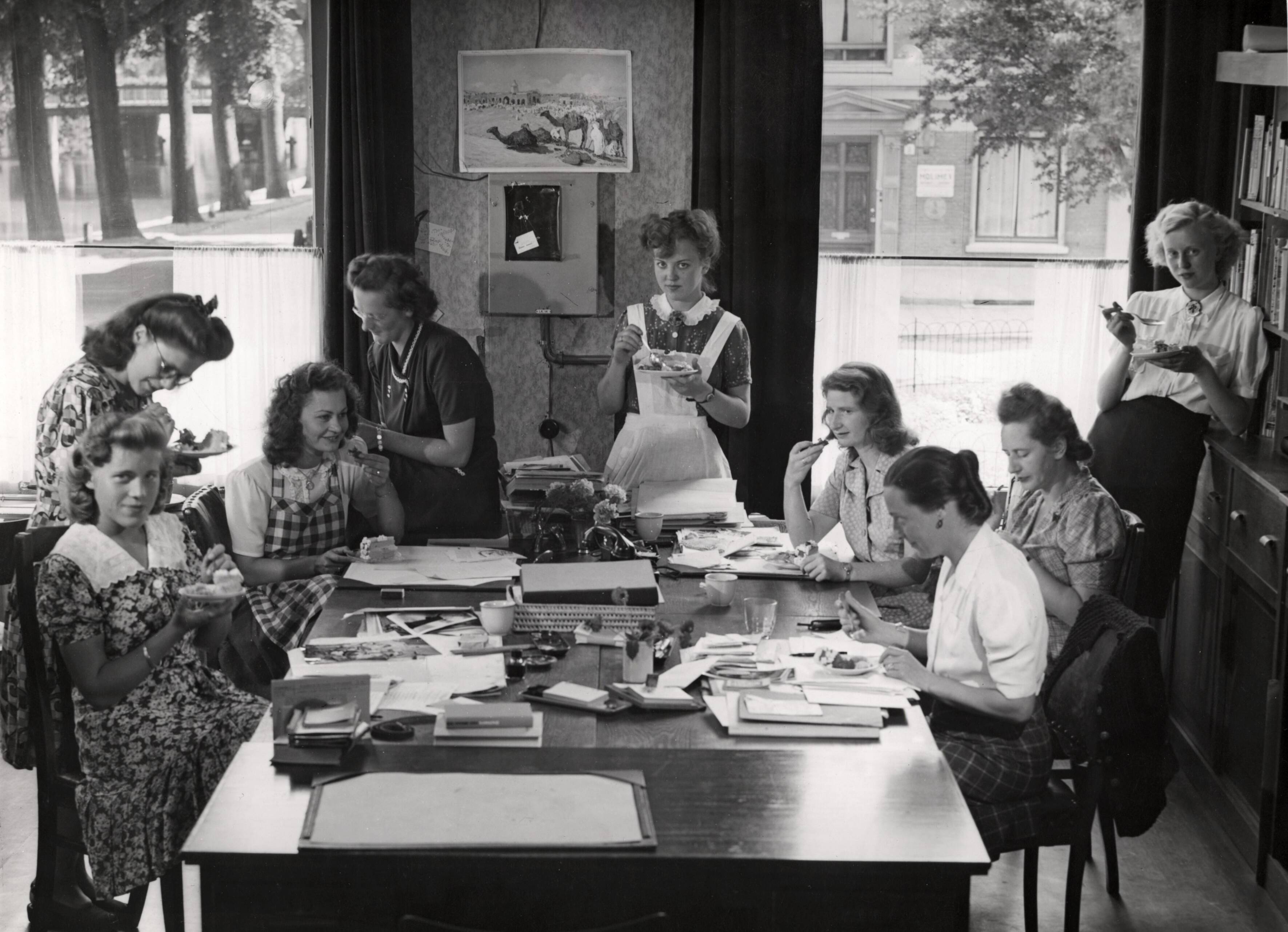 Voedsel — Redactrices van Libelle eten een taartje tijdens de koffiepauze. De redactie is gevestigd aan de Nassaulaan in Haarlem. Vierde van links in donkere japon Sanne van Liemt. 1947 — Foto: Hilterman, H. / Spaarnestad / Spaarnestad Photo (05887). Licentie: Set B: Rechtenvrij / Publiek Domein. Bron: Nationaal Archief. http://hdl.handle.net/10648/35429da6-3807-a382-e063-6df0900a6686