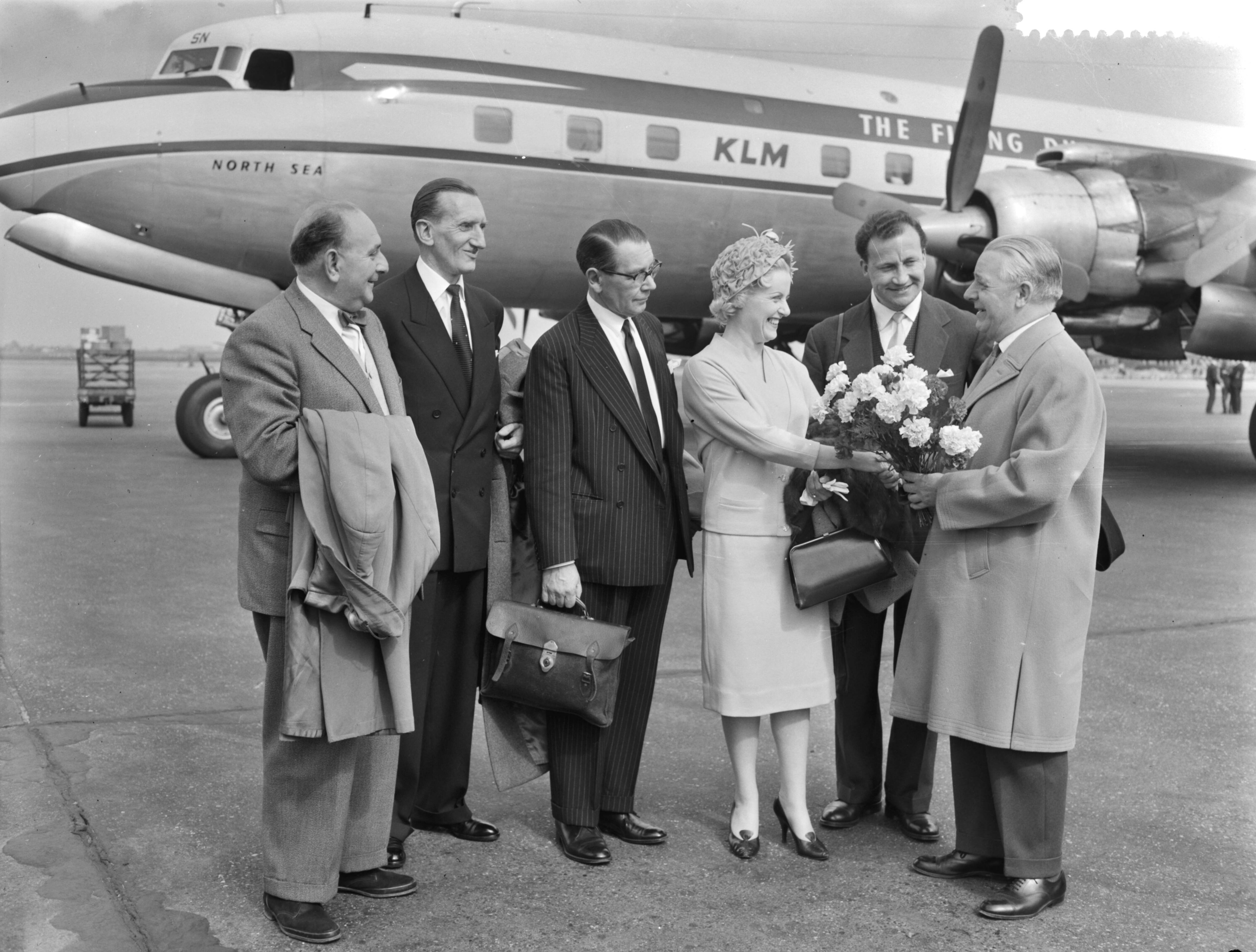 Fotocollectie Anefo — Aankomst op Schiphol van enkele leden van het BBC Concertorchestra, o.lv. Frank Wade, hoofd afdeling lichte muziek. V.l.n.r. Vilem Tausky (dirigent) , Sidney Torch (gastdirigent), BBC nieuwsomroeper Frank Phillips, Doreen Hume en John Lawrence. Doreen Hume krijgt bloemen aangeboden door mr. P.J. Mijksenaar, hoofd Public Relations van de gemeente Amsterdam — Foto: Rossem, Wim van / Anefo. Licentie: Set B: Rechtenvrij / Publiek Domein. Bron: Nationaal Archief. http://hdl.handle.net/10648/a9924530-d0b4-102d-bcf8-003048976d84