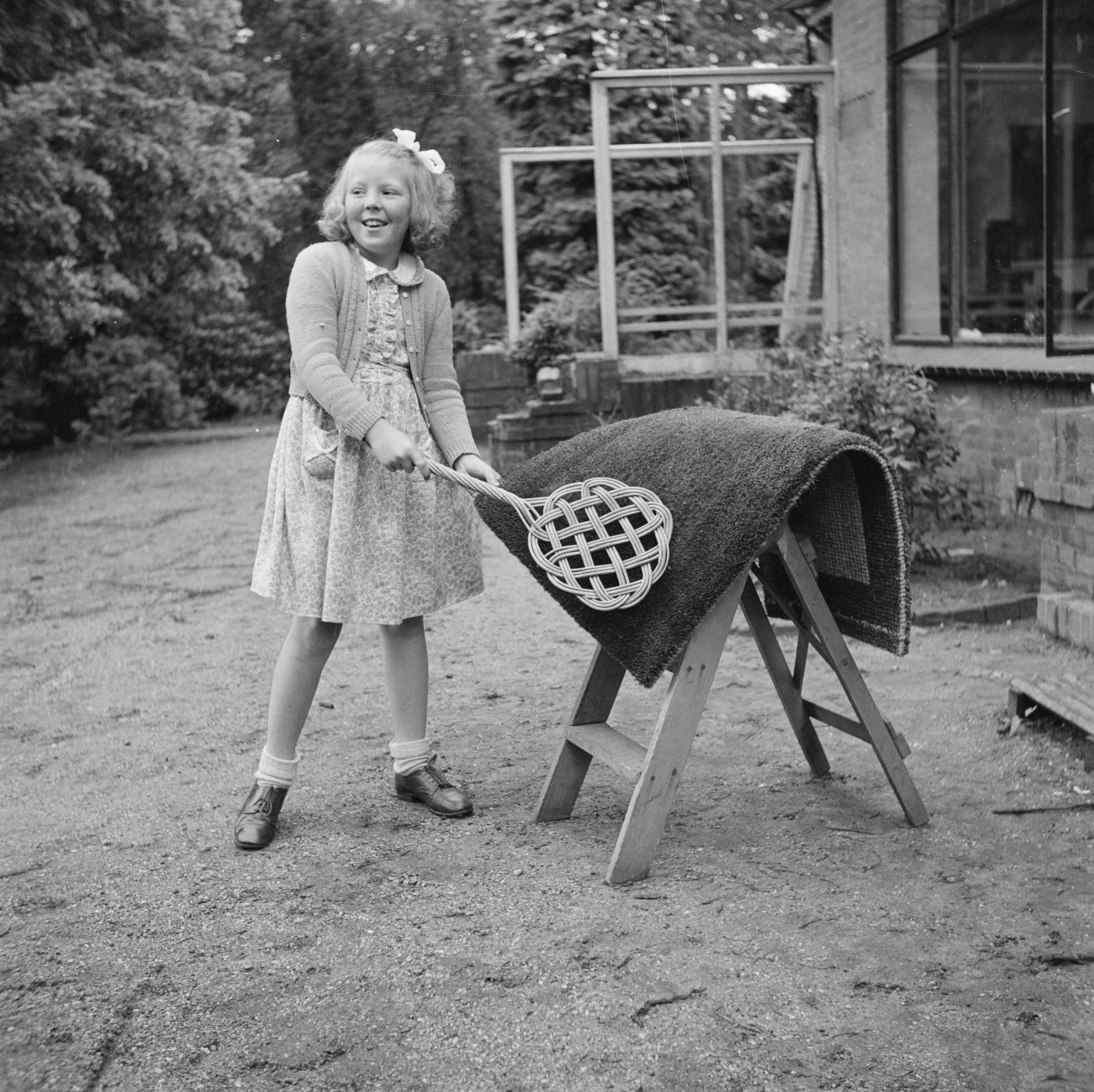 Prinses Beatrix en prinses Irene op de Werkplaats Kindergemeenschap van Kees Boeke te Bilthoven — Prinses Beatrix klopt een deurmat — Foto: Poll, Willem van de. Licentie: Set B: Rechtenvrij / Publiek Domein. Bron: Nationaal Archief. http://hdl.handle.net/10648/aee82540-d0b4-102d-bcf8-003048976d84