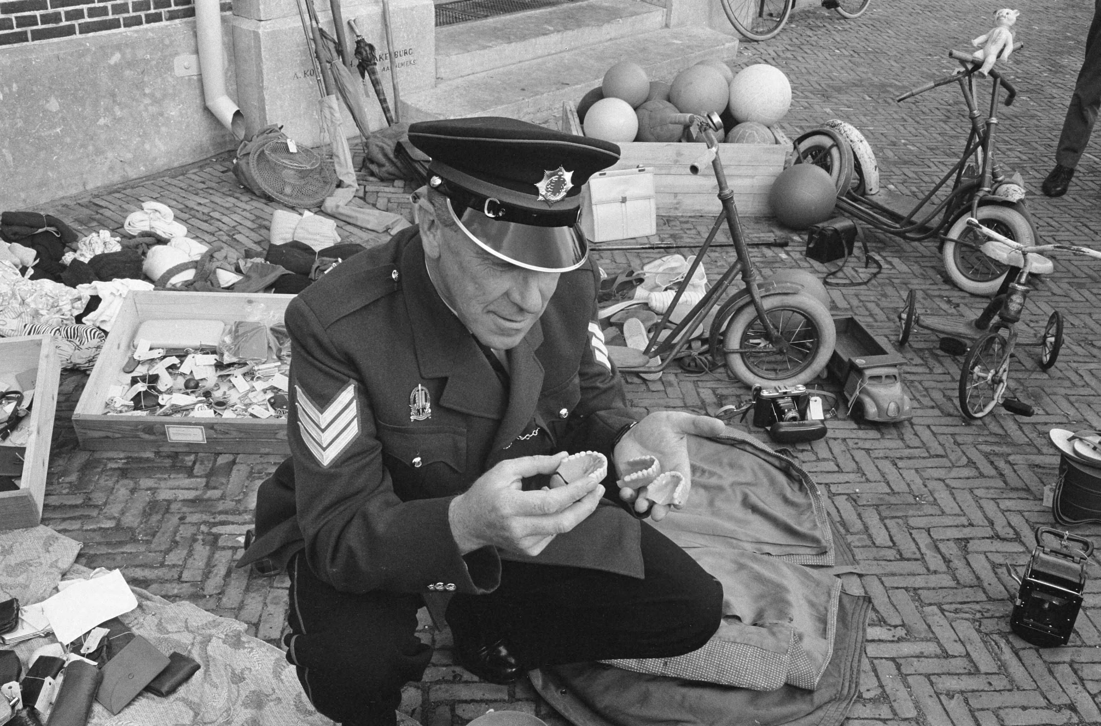 Fotocollectie Anefo — Einde zomerseizoen in Zandvoort. Politieagent sorteert de gevonden voorwerpen. In zijn handen kunstgebitten — Foto: Pot, Harry / Anefo. Licentie: Set B: Rechtenvrij / Publiek Domein. Bron: Nationaal Archief. http://hdl.handle.net/10648/a9e52070-d0b4-102d-bcf8-003048976d84