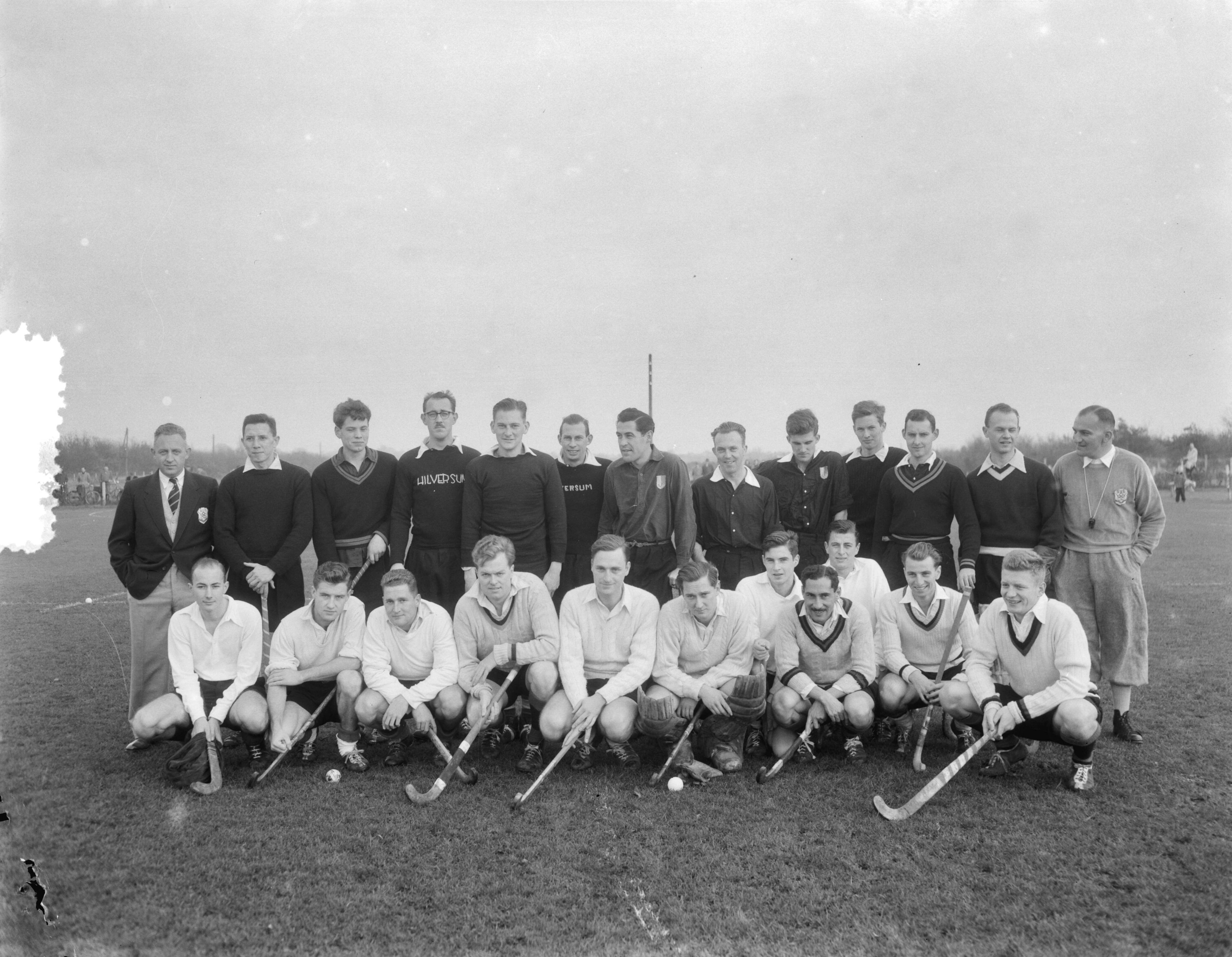 Fotocollectie Anefo — Huldiging hockeyer Dick Esser *gehurkt vierde van links, met snor). Laatste wedstrijd voor Amsterdam in een wedstrijd te Hilversum. Beide ploegen poseren — Foto: Duinen, G.W. van / Anefo. Licentie: Set B: Rechtenvrij / Publiek Domein. Bron: Nationaal Archief. http://hdl.handle.net/10648/a9185eaa-d0b4-102d-bcf8-003048976d84