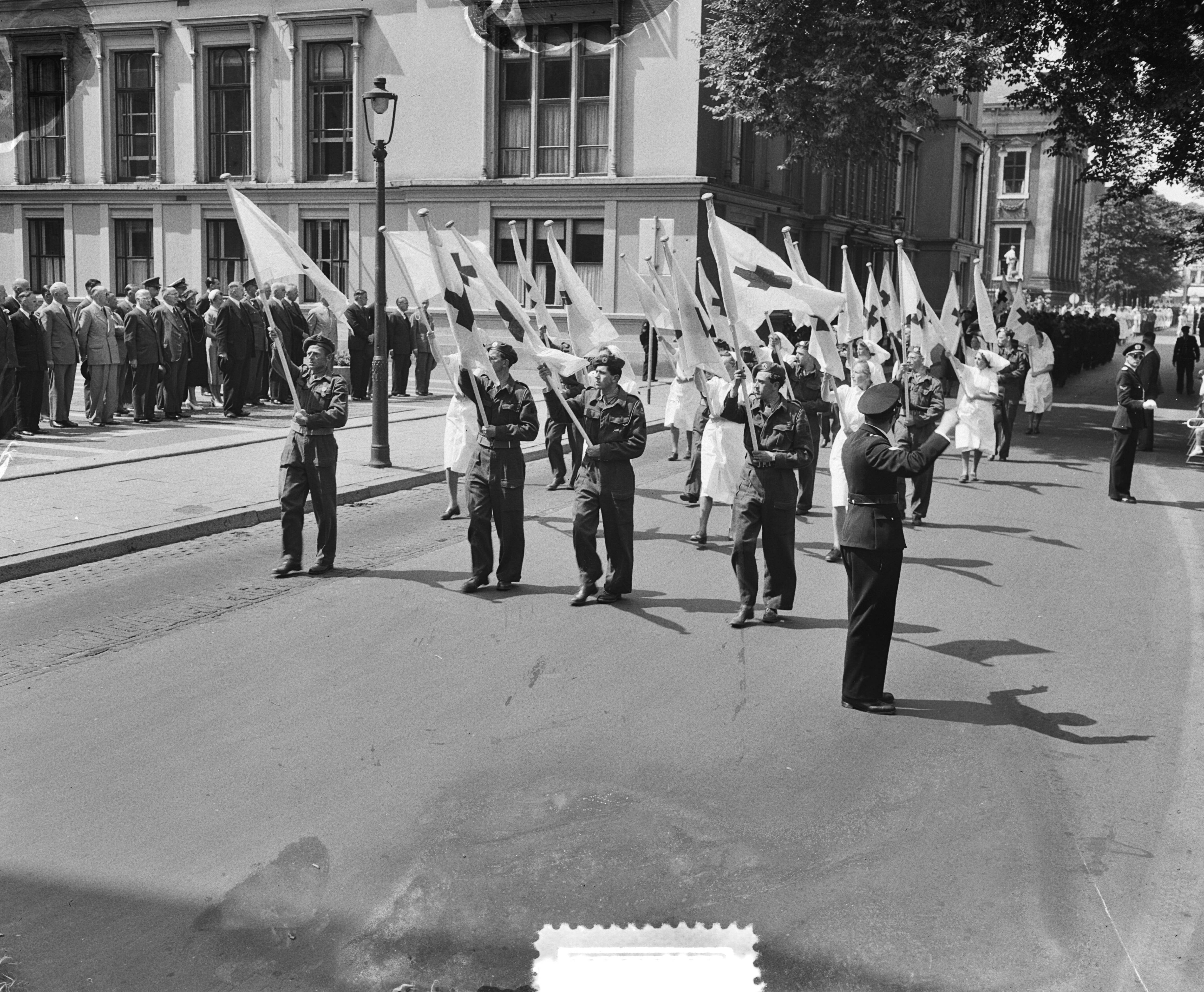 Fotocollectie Anefo — Defilé voor het hoofdbestuur van het Rode Kruis voor het gebouw van de Hoge Raad op het Plein te Den Haag. Vlaggendragers — Foto: Consenheim, Wim / Anefo. Licentie: Set B: Rechtenvrij / Publiek Domein. Bron: Nationaal Archief. http://hdl.handle.net/10648/a8fc2c1c-d0b4-102d-bcf8-003048976d84