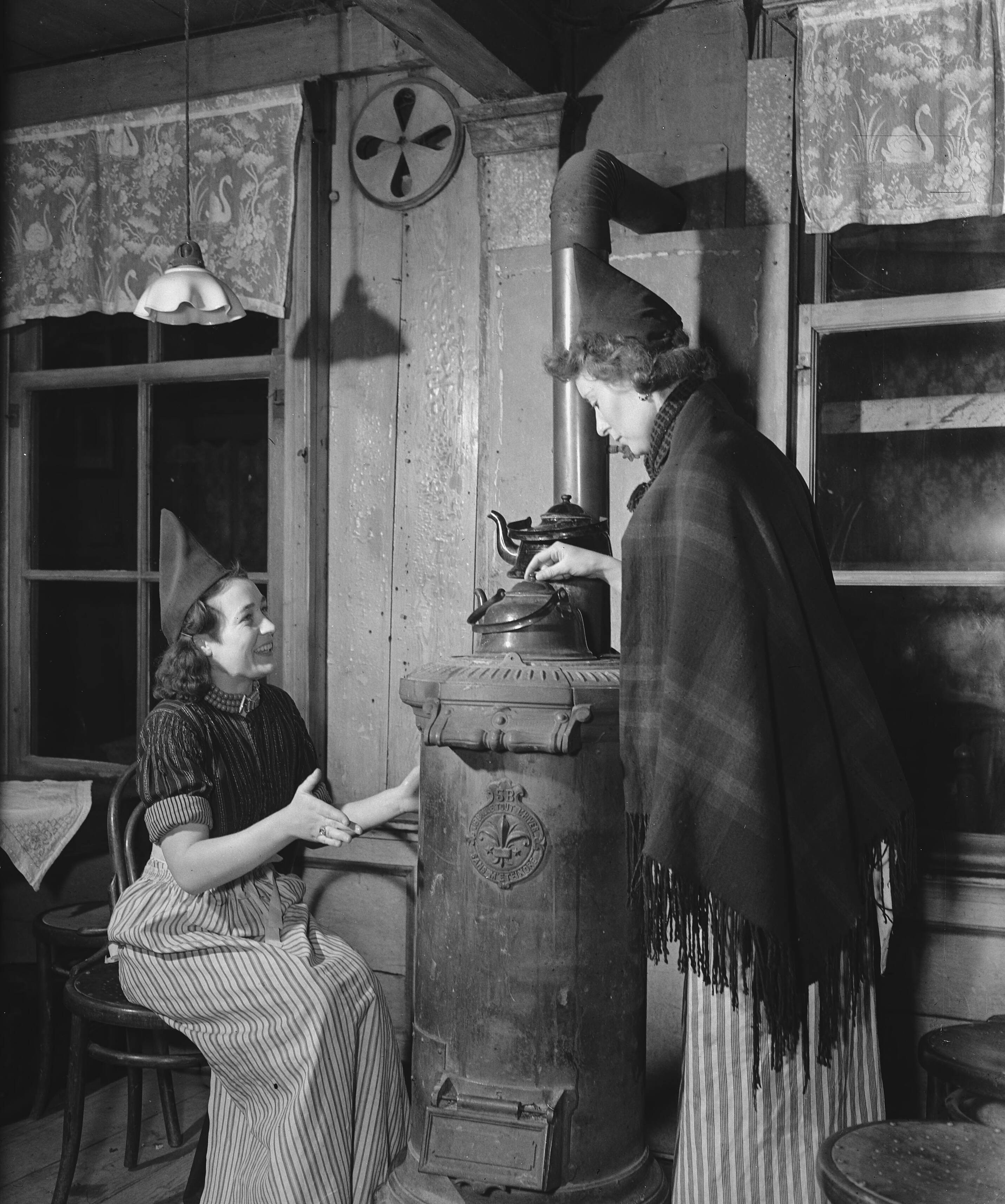Volendam op de schaats — [Twee vrouwen bij een kachel] — Foto: Raucamp, Koos / Anefo. Licentie: Set B: Rechtenvrij / Publiek Domein. Bron: Nationaal Archief. http://hdl.handle.net/10648/a89601da-d0b4-102d-bcf8-003048976d84