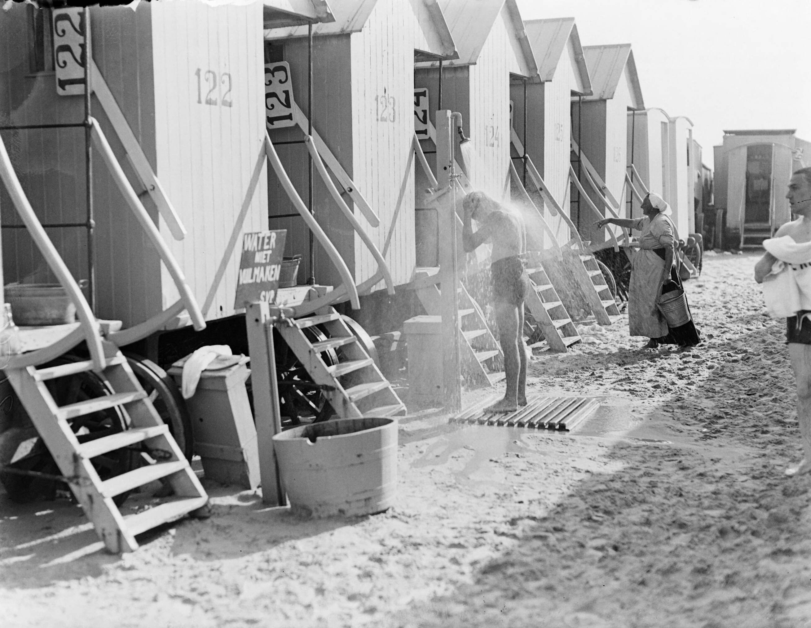 Strandtaferelen Scheveningen — Jongen neemt douche tussen badkoetsen — Foto: Poll, Willem van de. Licentie: Set B: Rechtenvrij / Publiek Domein. Bron: Nationaal Archief. http://hdl.handle.net/10648/aea8622a-d0b4-102d-bcf8-003048976d84