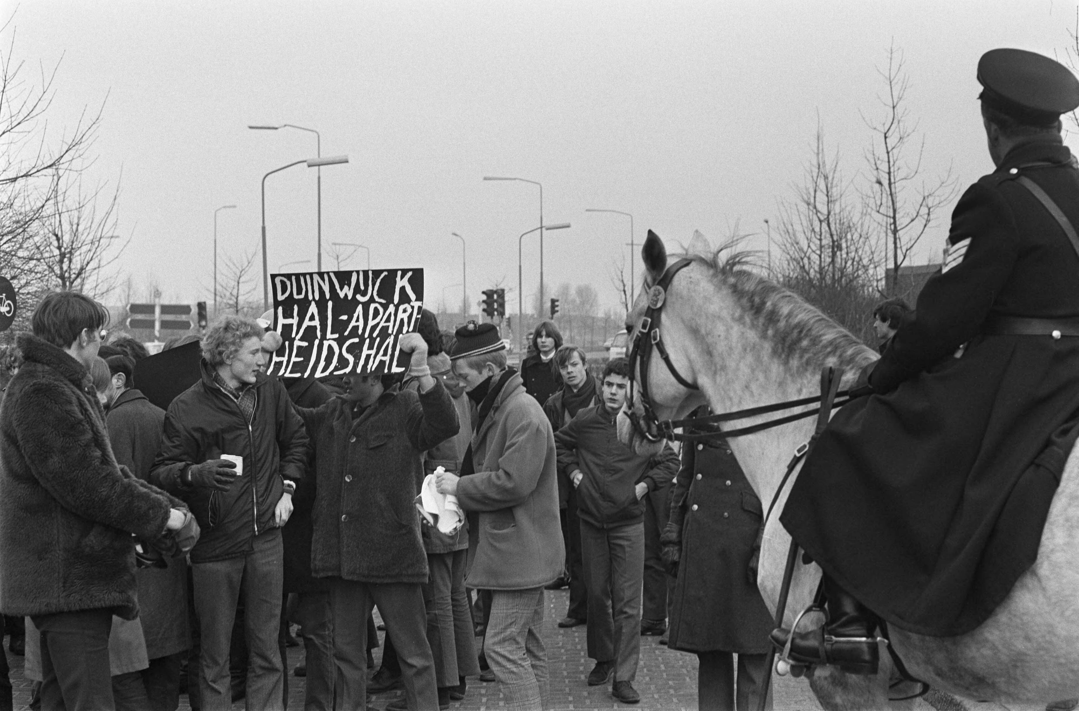 Fotocollectie Anefo — Demonstranten met spandoeken tegen deelname van Zuid-Afrikaanse spelers bij Duinwijckhal Haarlem — Foto: Evers, Joost / Anefo. Licentie: Set B: Rechtenvrij / Publiek Domein. Bron: Nationaal Archief. http://hdl.handle.net/10648/ab8d4f60-d0b4-102d-bcf8-003048976d84